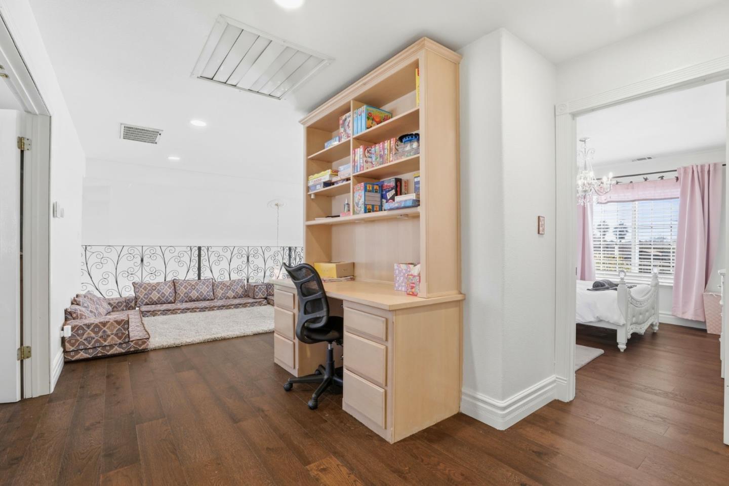 Furnished office and sitting area with built-in desk, patterned sofa, and an adjoining bedroom.