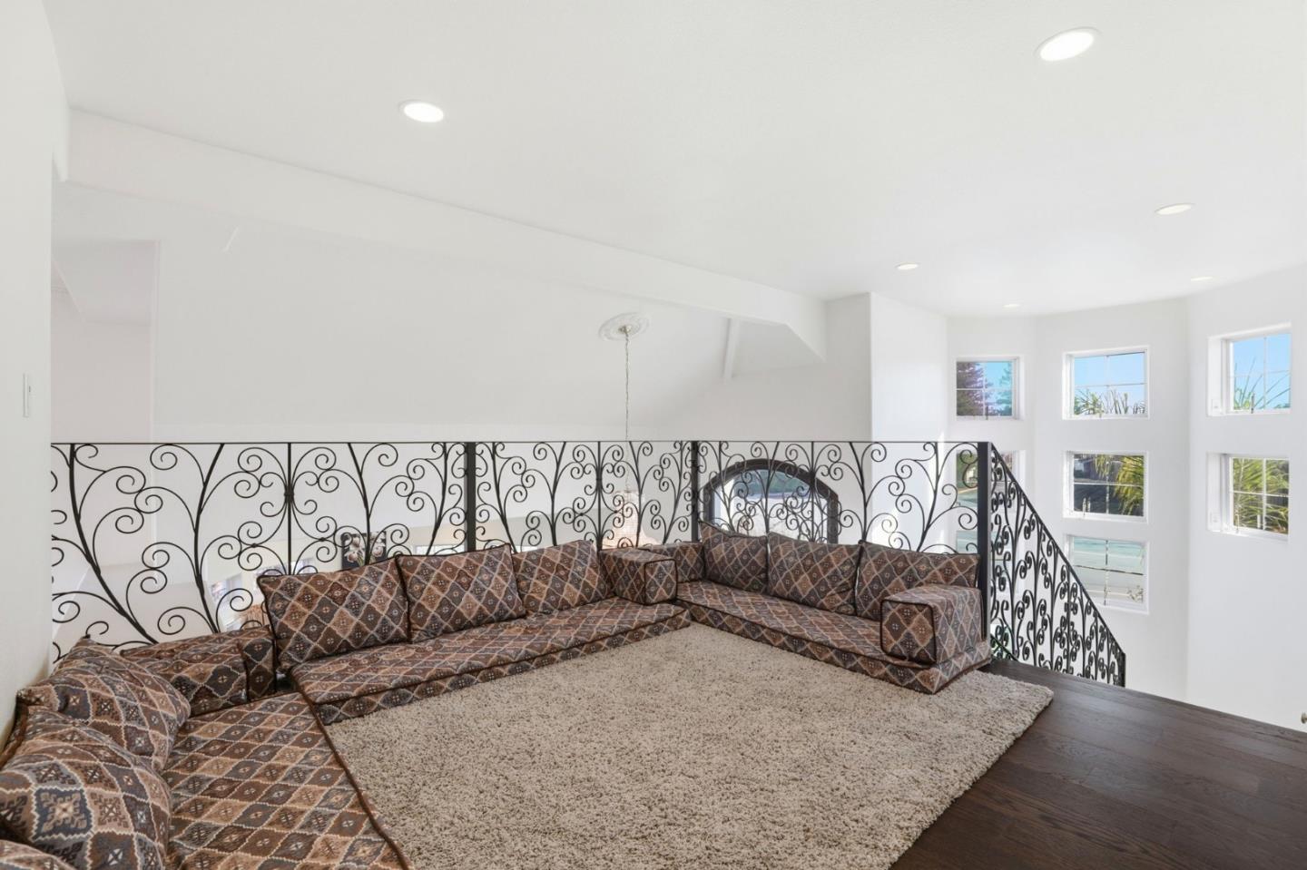 Furnished loft sitting area with patterned sectional, ornate iron railing, and tall windows.