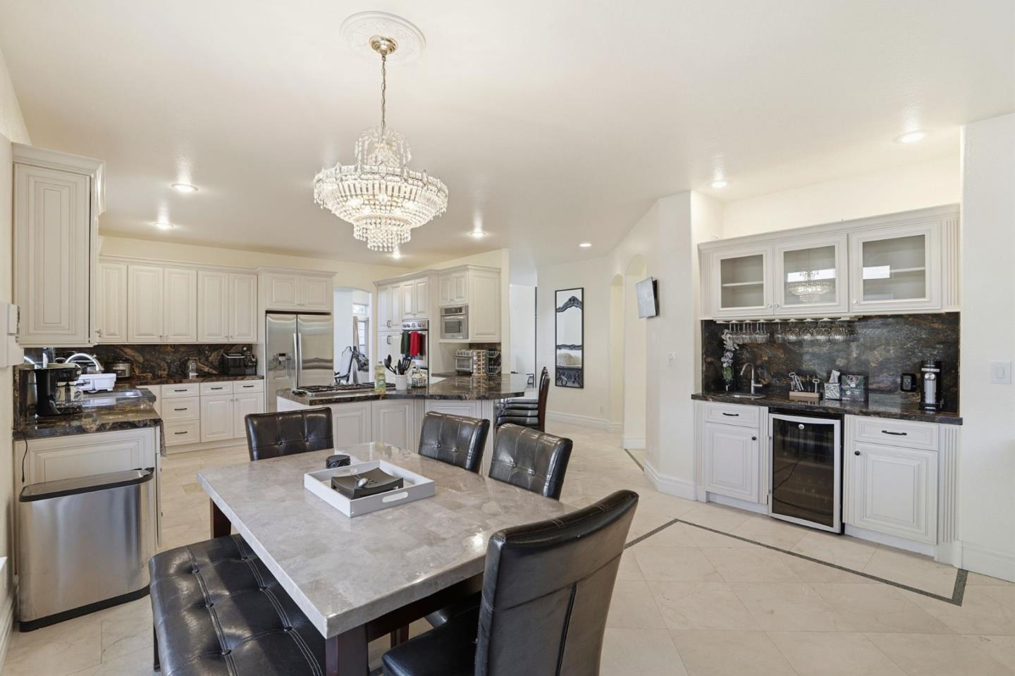 Spacious kitchen with white cabinetry, dark stone counters, stainless appliances, and a crystal chandelier.