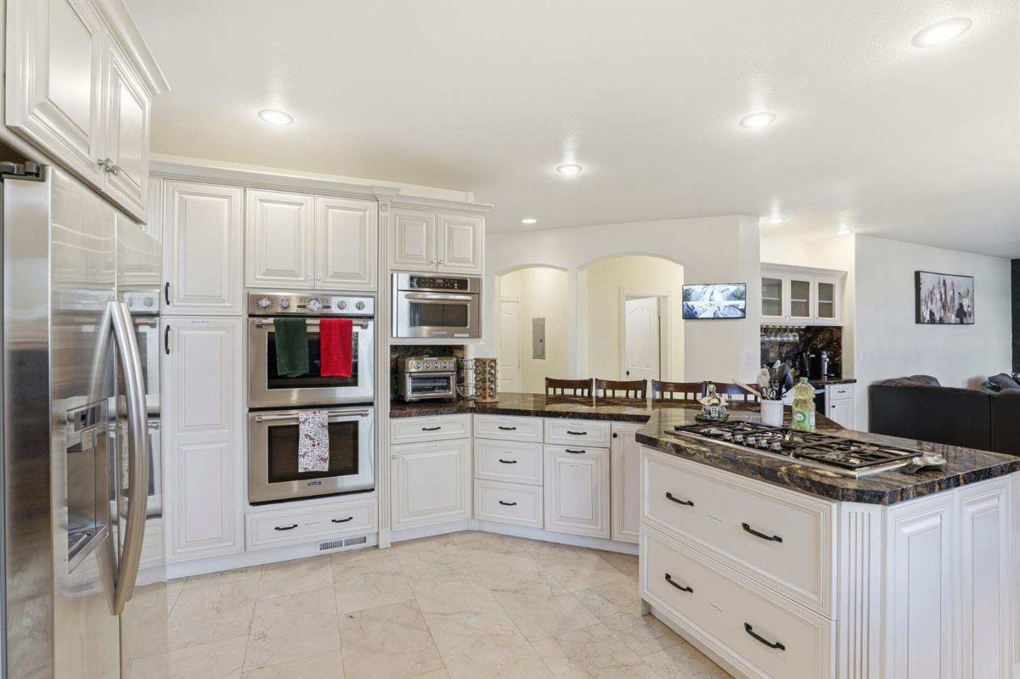Bright kitchen with white cabinetry, stainless steel double ovens, and a dark stone island with gas cooktop.