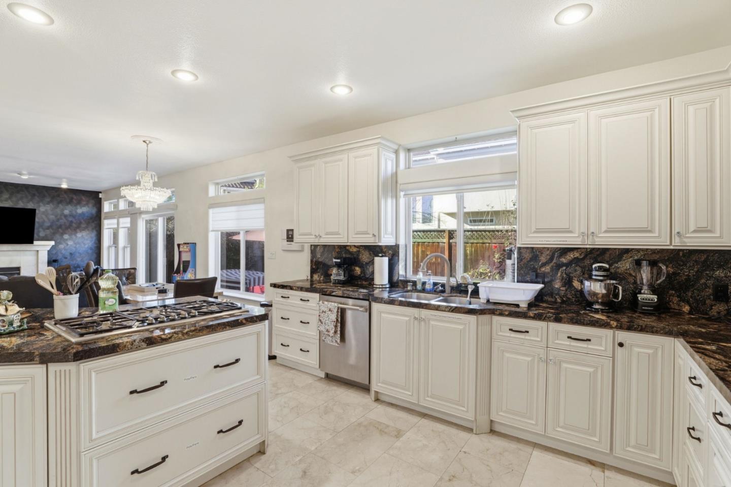 Kitchen with white paneled cabinets, dark granite counters, a gas cooktop island, and windows facing the yard.