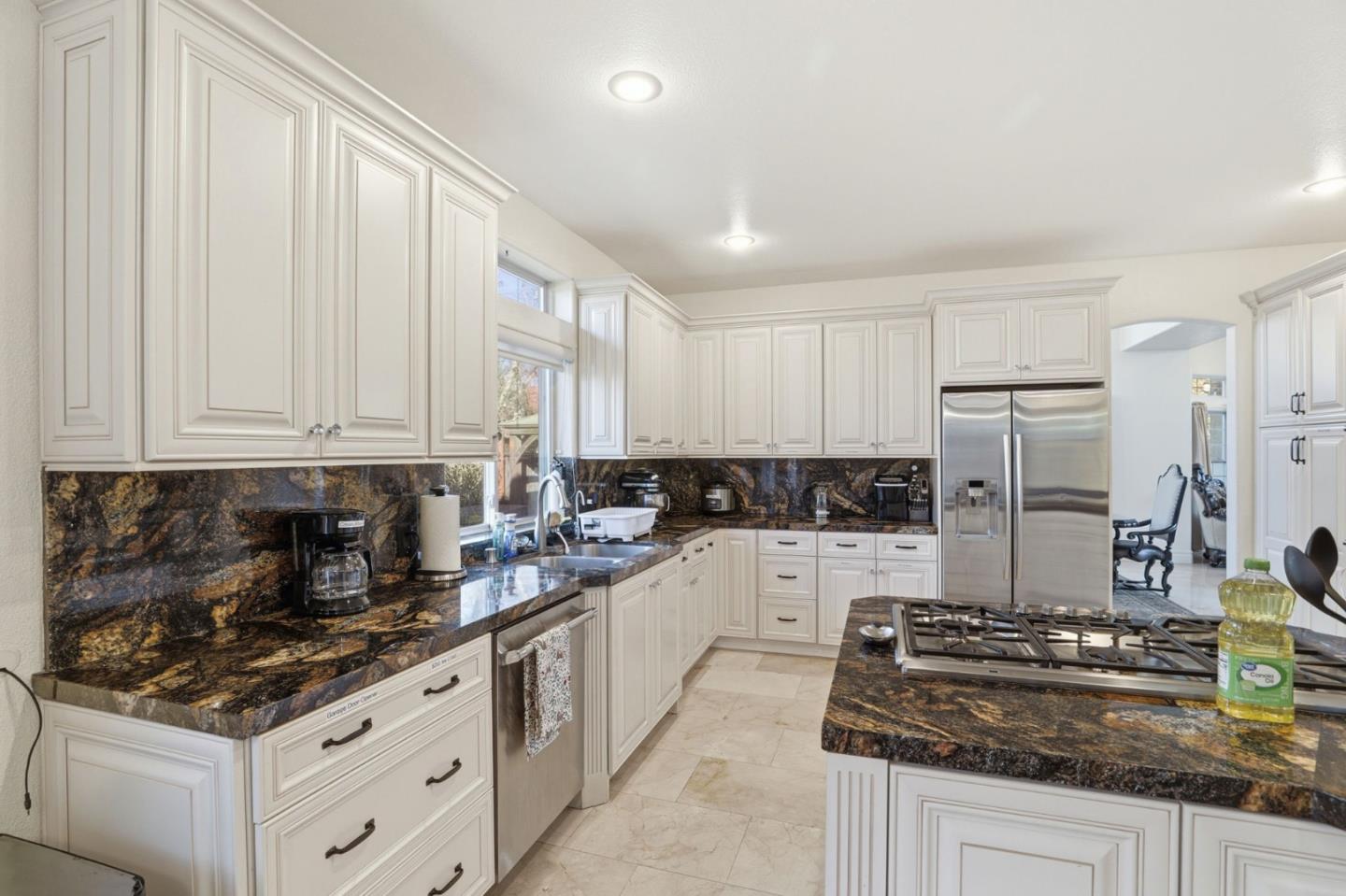 Kitchen with white cabinetry, dark granite counters, a large cooktop island, and stainless steel refrigerator.
