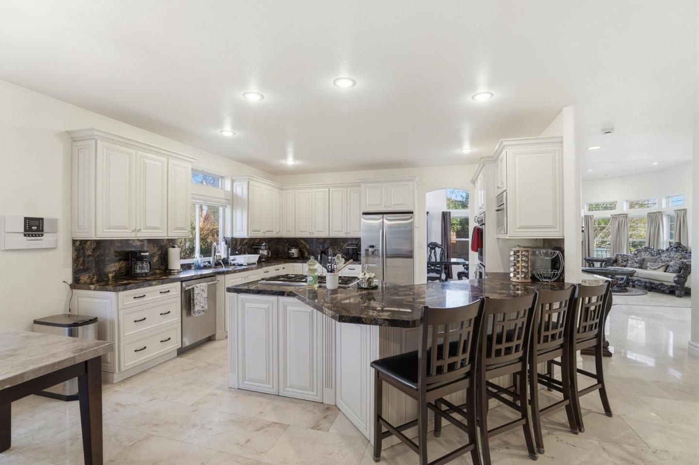 Kitchen with white cabinetry, dark stone island and counters, stainless steel appliances, and a row of bar stools.