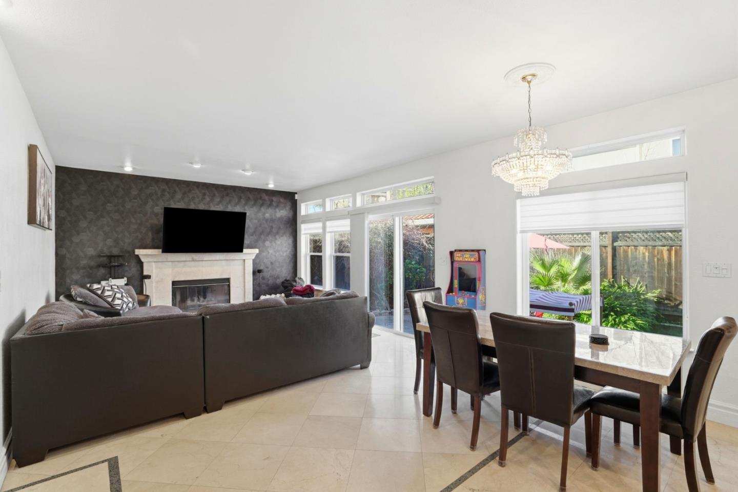 Living and dining room with a fireplace, chandelier, and large windows overlooking a garden.