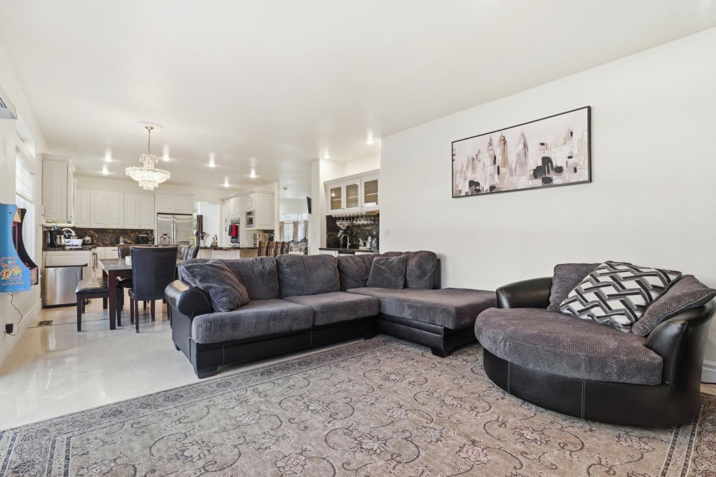 Open-plan living room with a large gray sectional, round lounge chair, and kitchen with white cabinets.