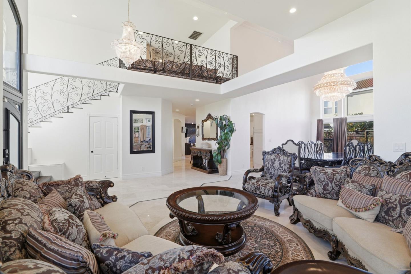 Living room with ornate sofas, crystal chandeliers, and a wrought-iron staircase overlooking the space.