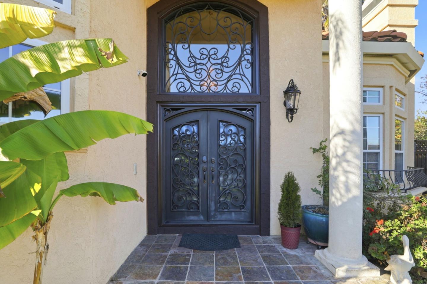Home entrance with ornate wrought-iron double doors, tiled porch, and white column.