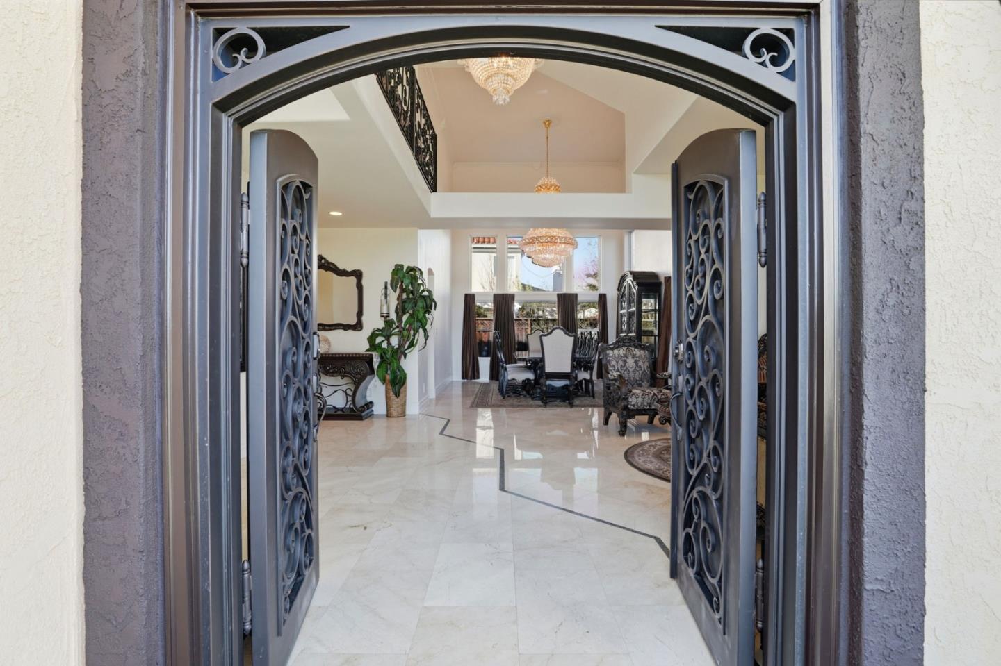 Grand foyer with ornate open entry doors, marble floors, chandeliers, and a formal dining area.