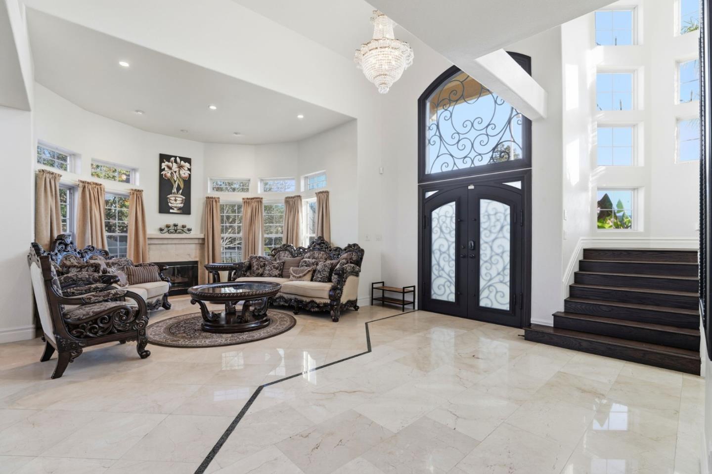 Furnished foyer with ornate living room seating, a tall decorative front door, marble floors, and a dark staircase.