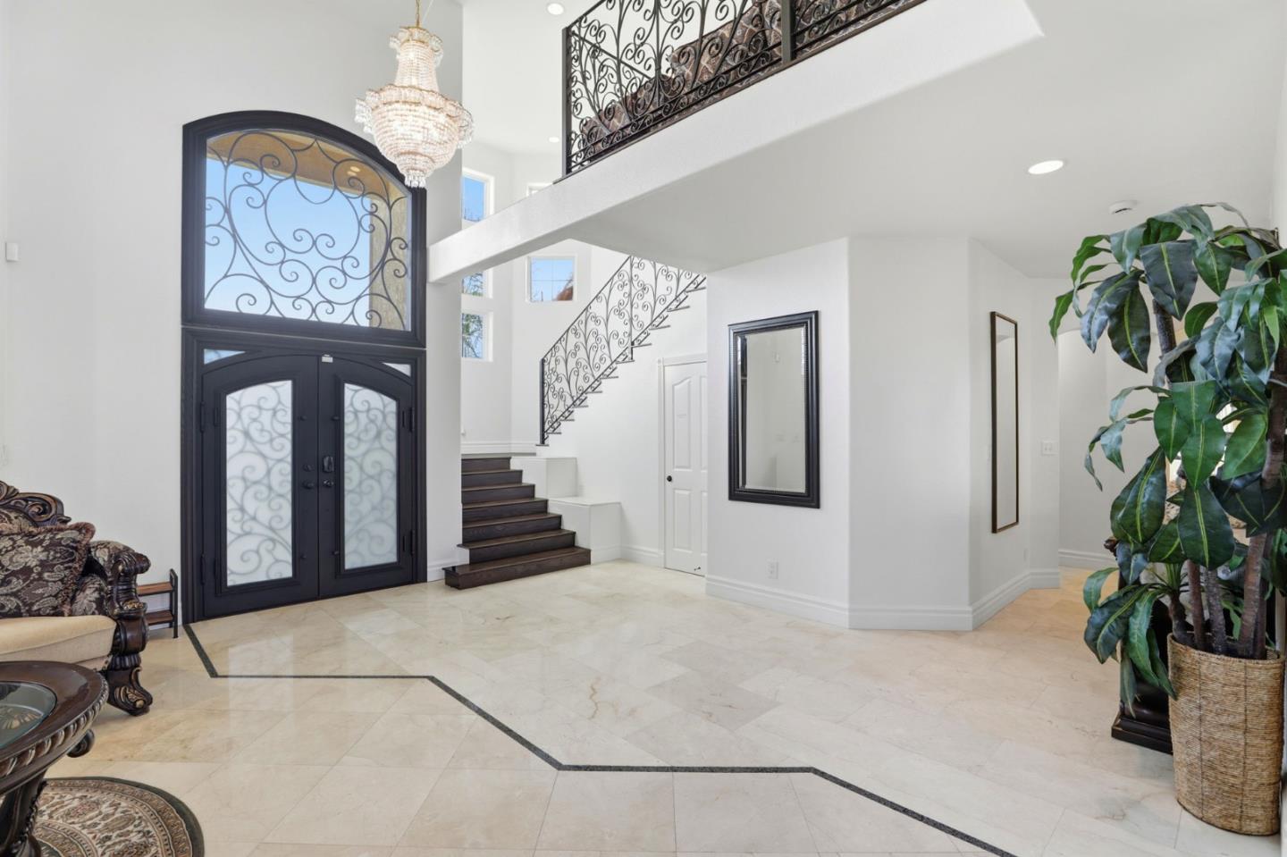 Two-story foyer with ornate glass entry doors, a crystal chandelier, marble floors, and an iron-railed staircase.