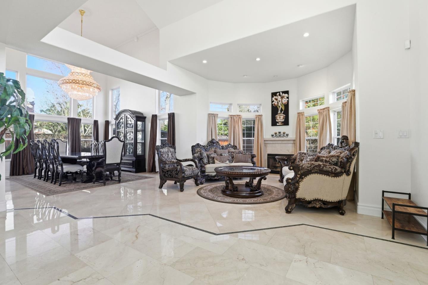 Open-plan living and dining room with ornate furnishings, a fireplace, and glossy marble floors.