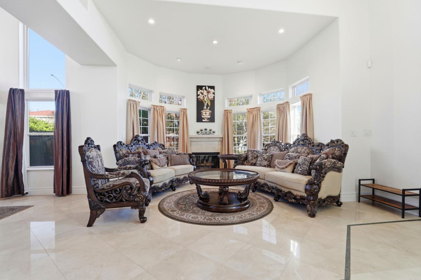 Furnished living room with ornate carved seating, tall windows, and glossy tile floors.