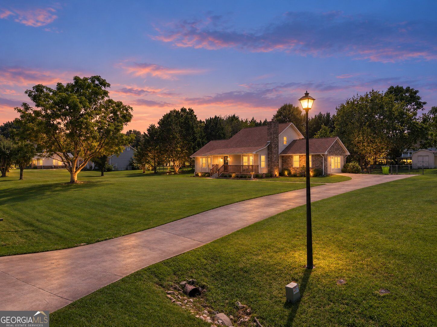 Detached home with a stone chimney and lit windows beside a walkway at dusk.