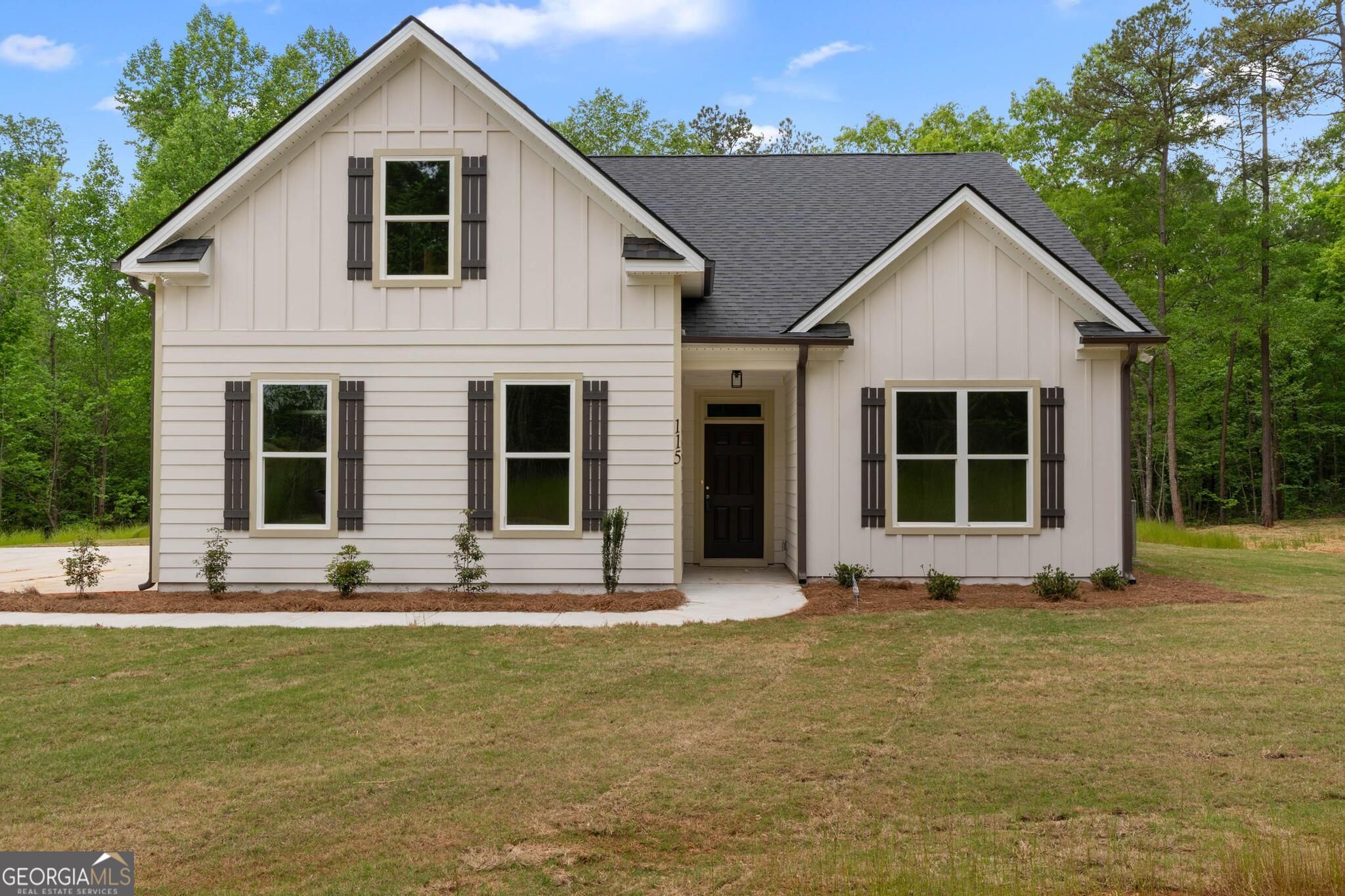 Light-colored two-story home with dark shutters, covered entry, and a broad front lawn.