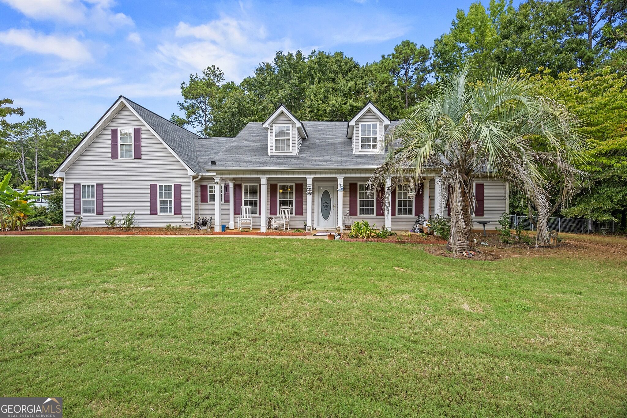 Gray two-story home with burgundy shutters, a covered porch, and palm trees beside a broad lawn.