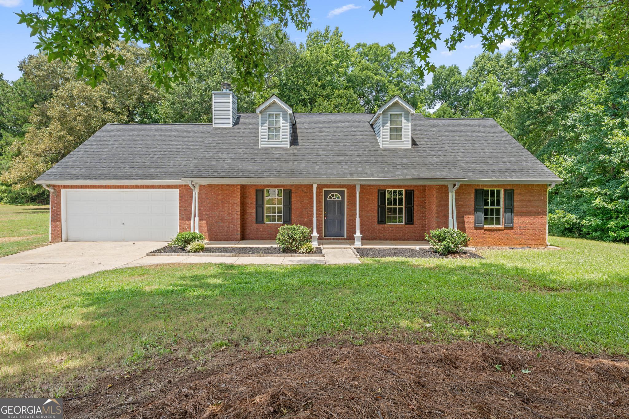Red-brick house with two roof dormers, a covered porch, and an attached garage.