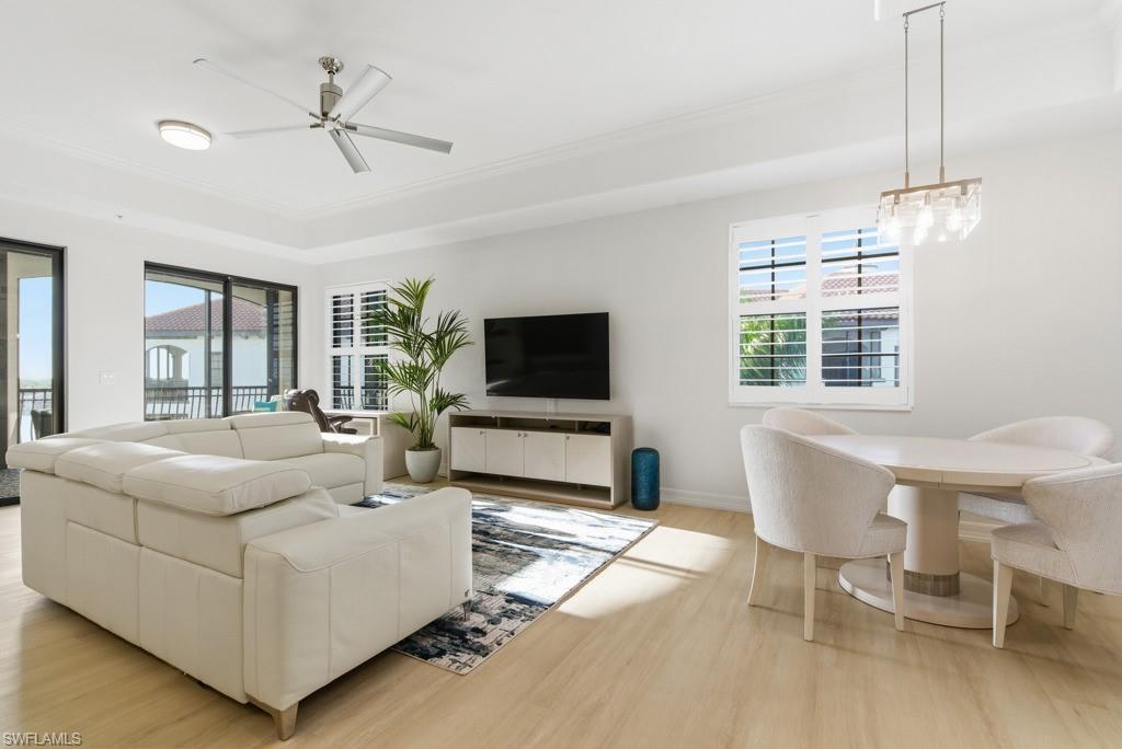 Open-plan living and dining room with white sofas, pale wood floors, and sliding glass doors to a balcony.