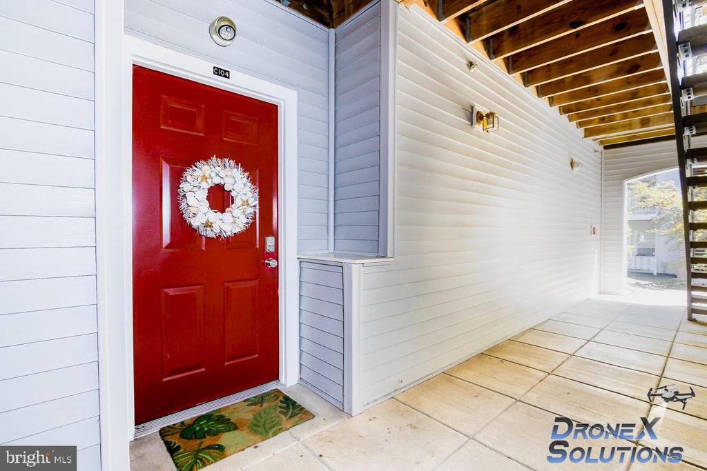 Covered exterior entrance with a red C104 door, white wreath, and tiled porch.