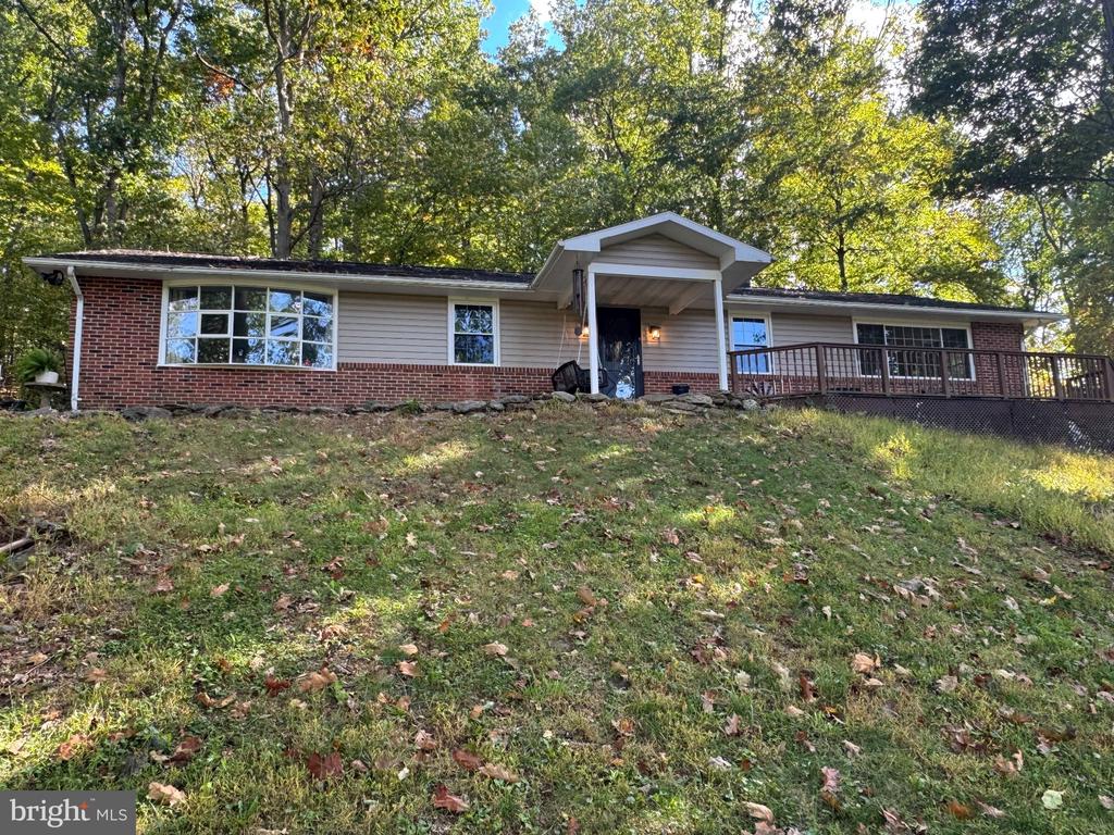 Single-story ranch home with a brick facade, covered entry, and long wooden deck beneath mature trees.