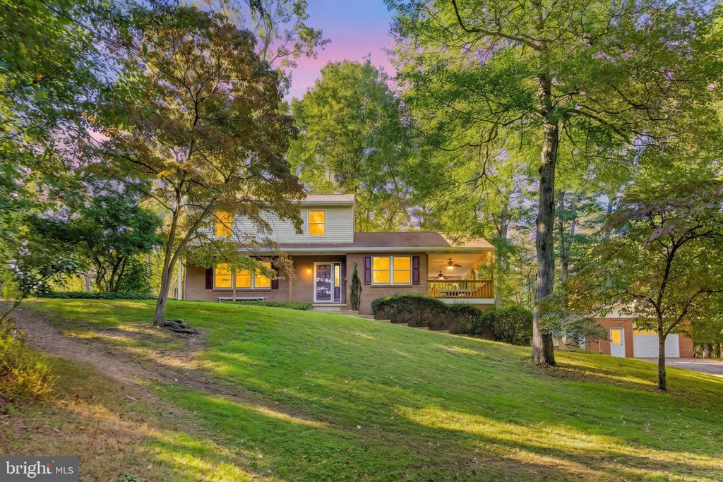 Two-story home with brick and siding, a covered porch, and mature trees at golden hour.