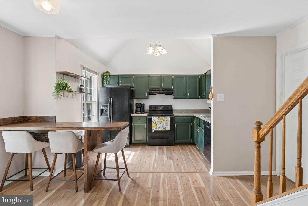Kitchen with dark green cabinets and a wooden dining table beside the staircase.