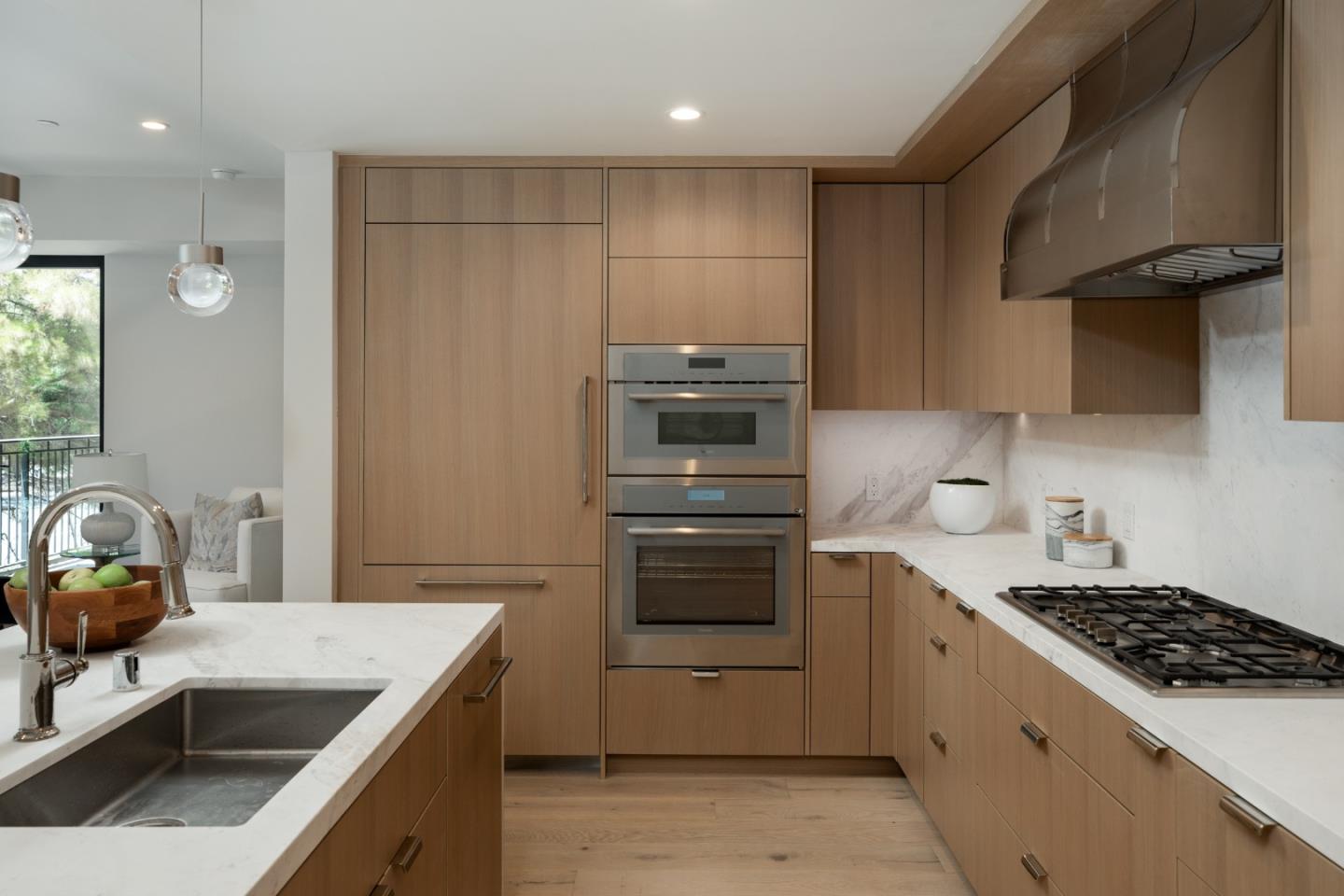 Modern kitchen with wood cabinetry, marble counters, double ovens, and a large island sink.