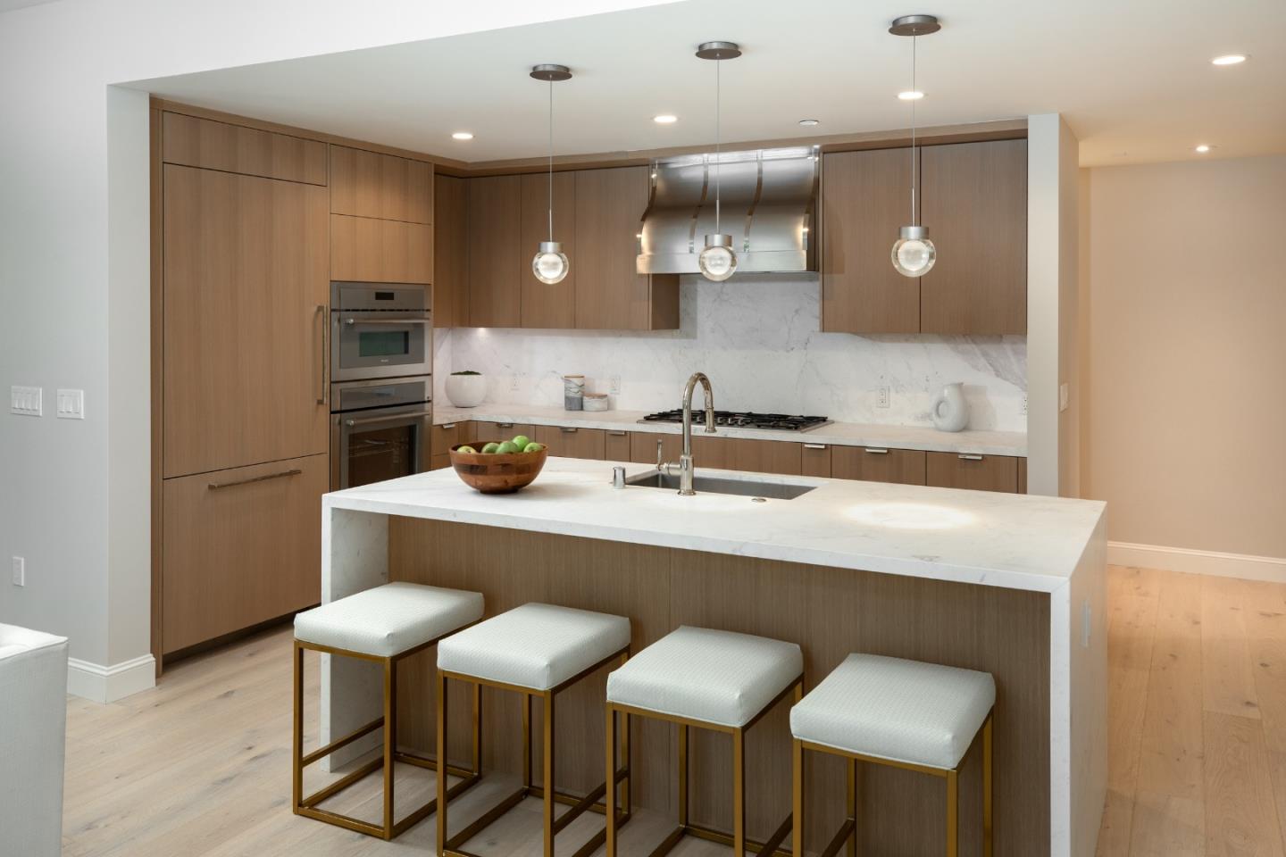 Modern kitchen with wood cabinetry, marble counters, and a large island with four stools.
