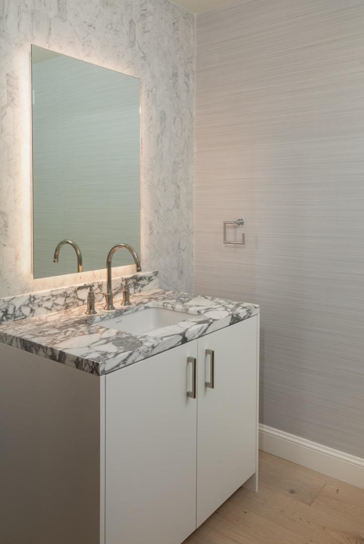 Bathroom vanity with a veined marble countertop, brass faucet, and illuminated mirror.
