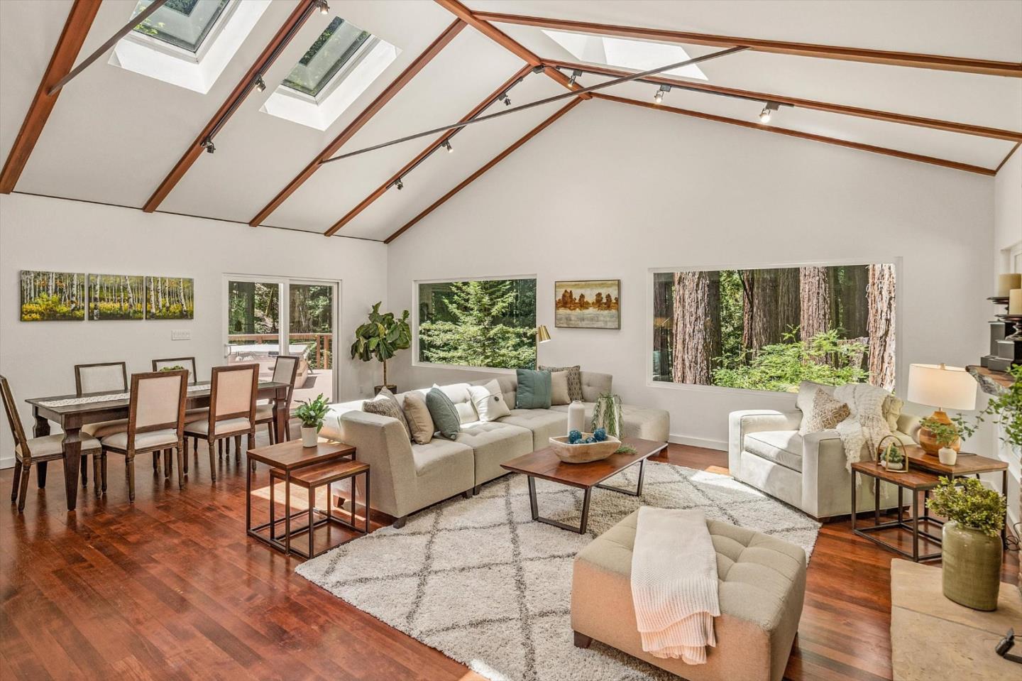 Living room with exposed wood ceiling beams, skylights, and windows overlooking trees.