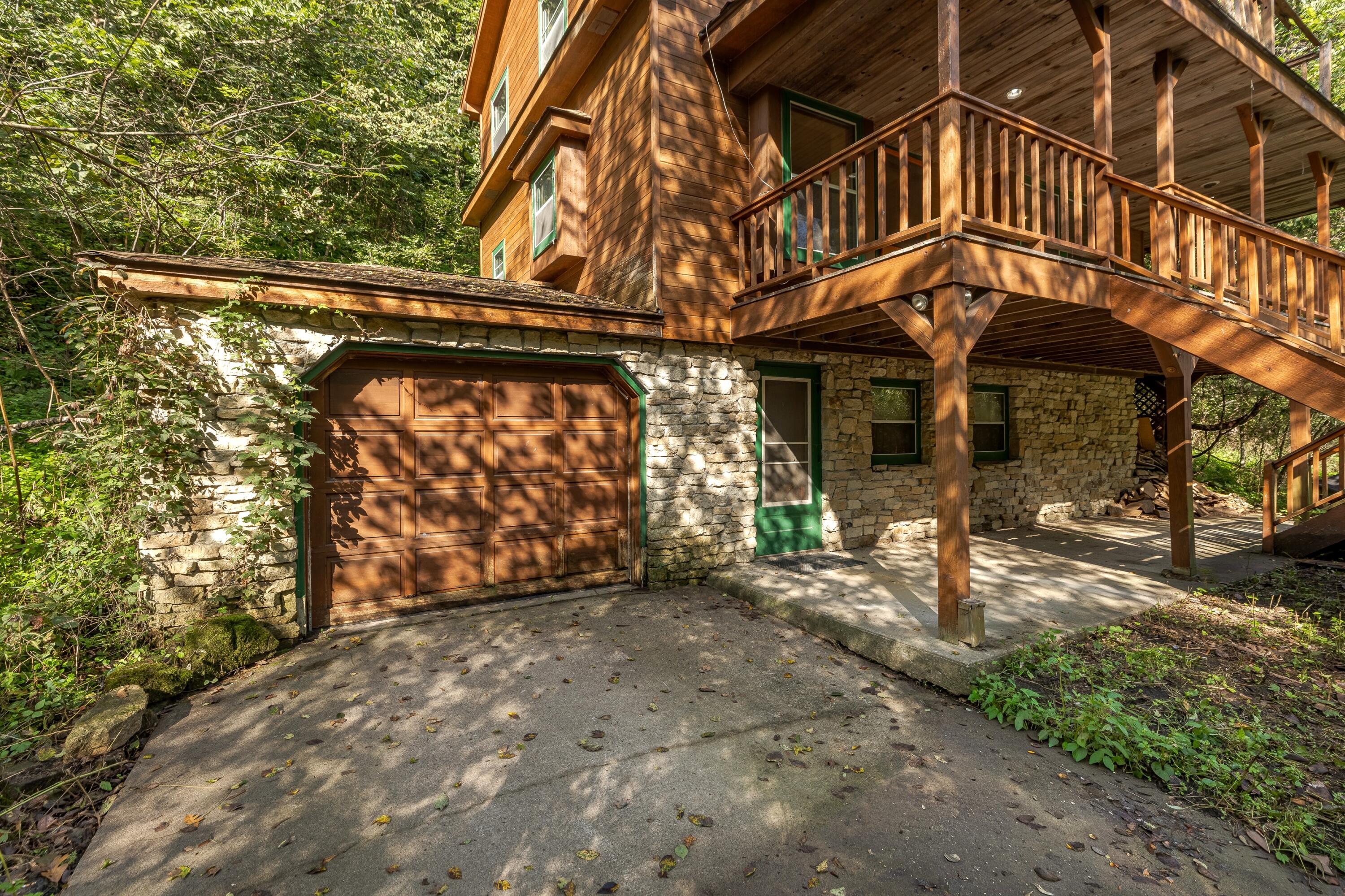 Wood-sided home with a stone lower level, brown garage door, and expansive raised deck in a wooded setting.