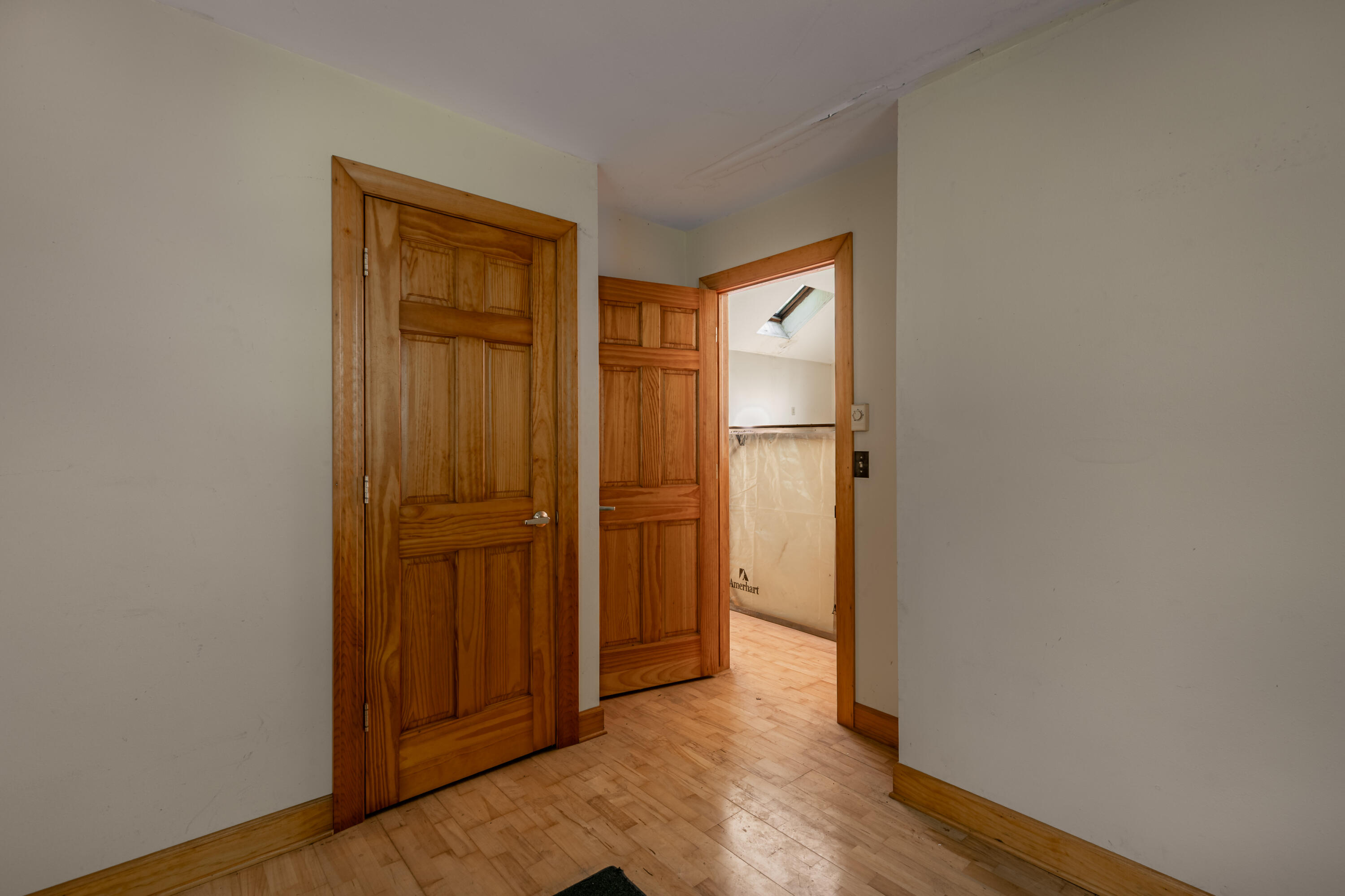 Empty hallway with wood floors and paneled wooden doors, opening to a room with a skylight.
