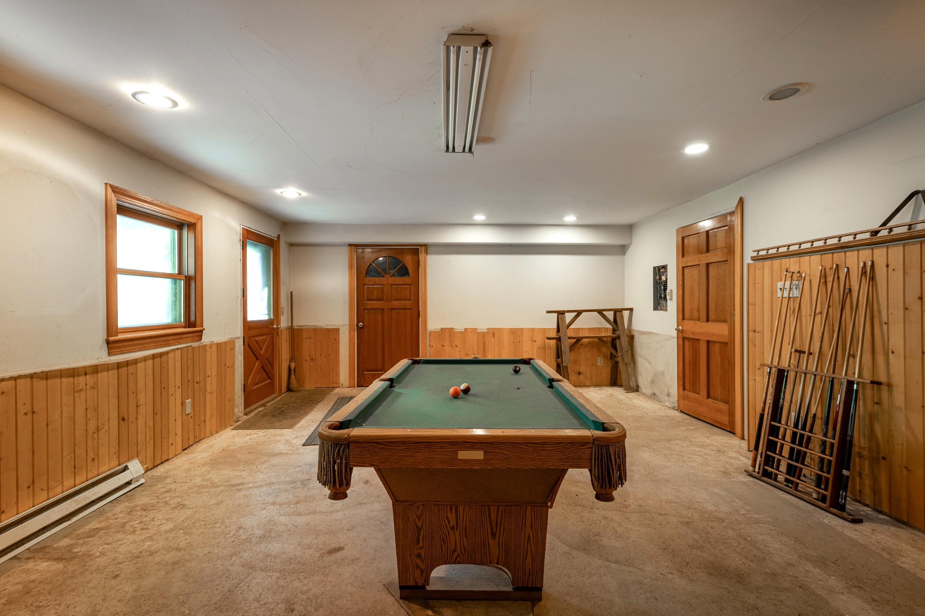 Recreation room with a green-felt pool table and a wall-mounted rack of pool cues.