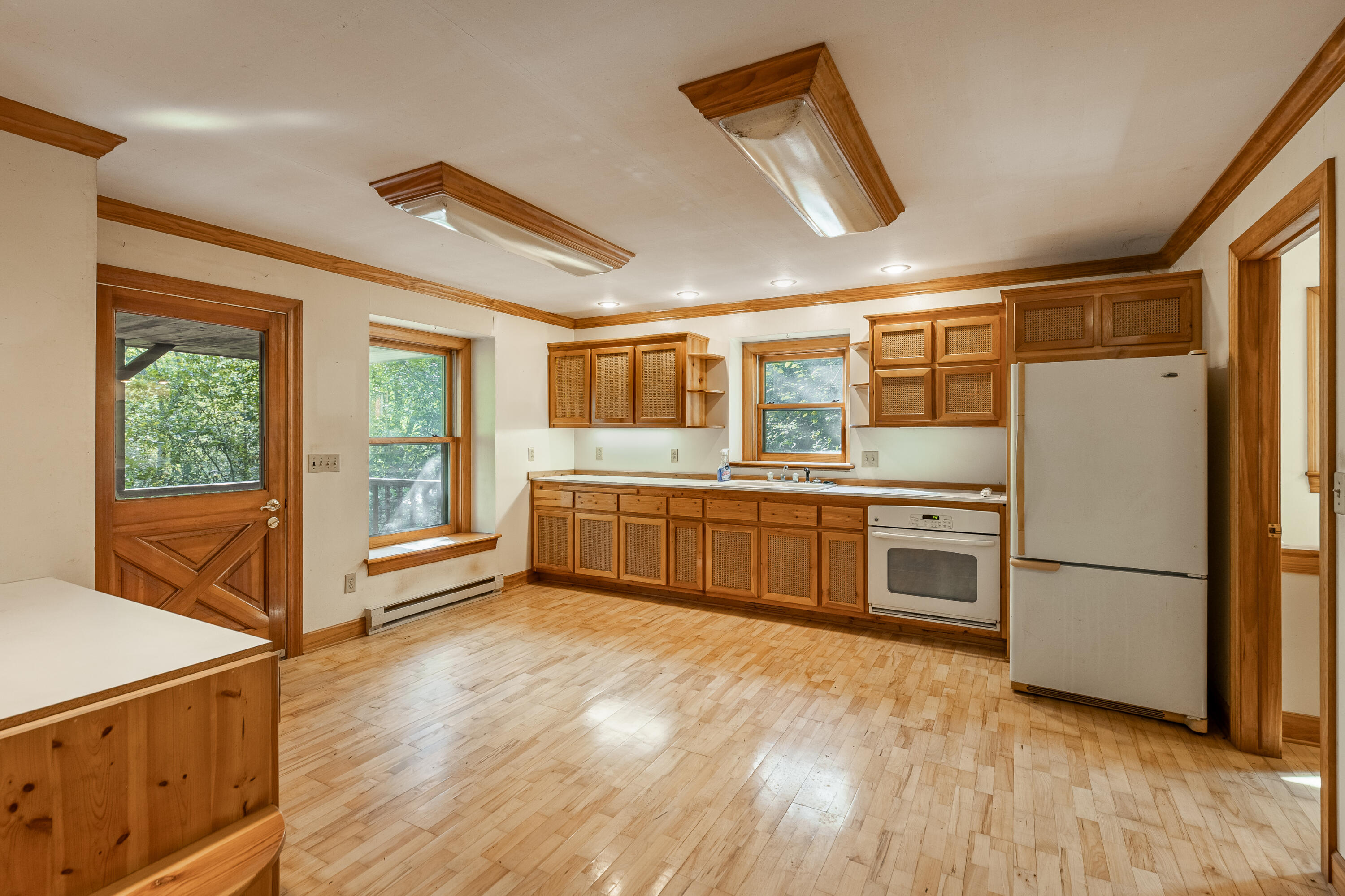 Vacant kitchen with warm wood cabinets, light hardwood floors, and a wood-framed exterior door.