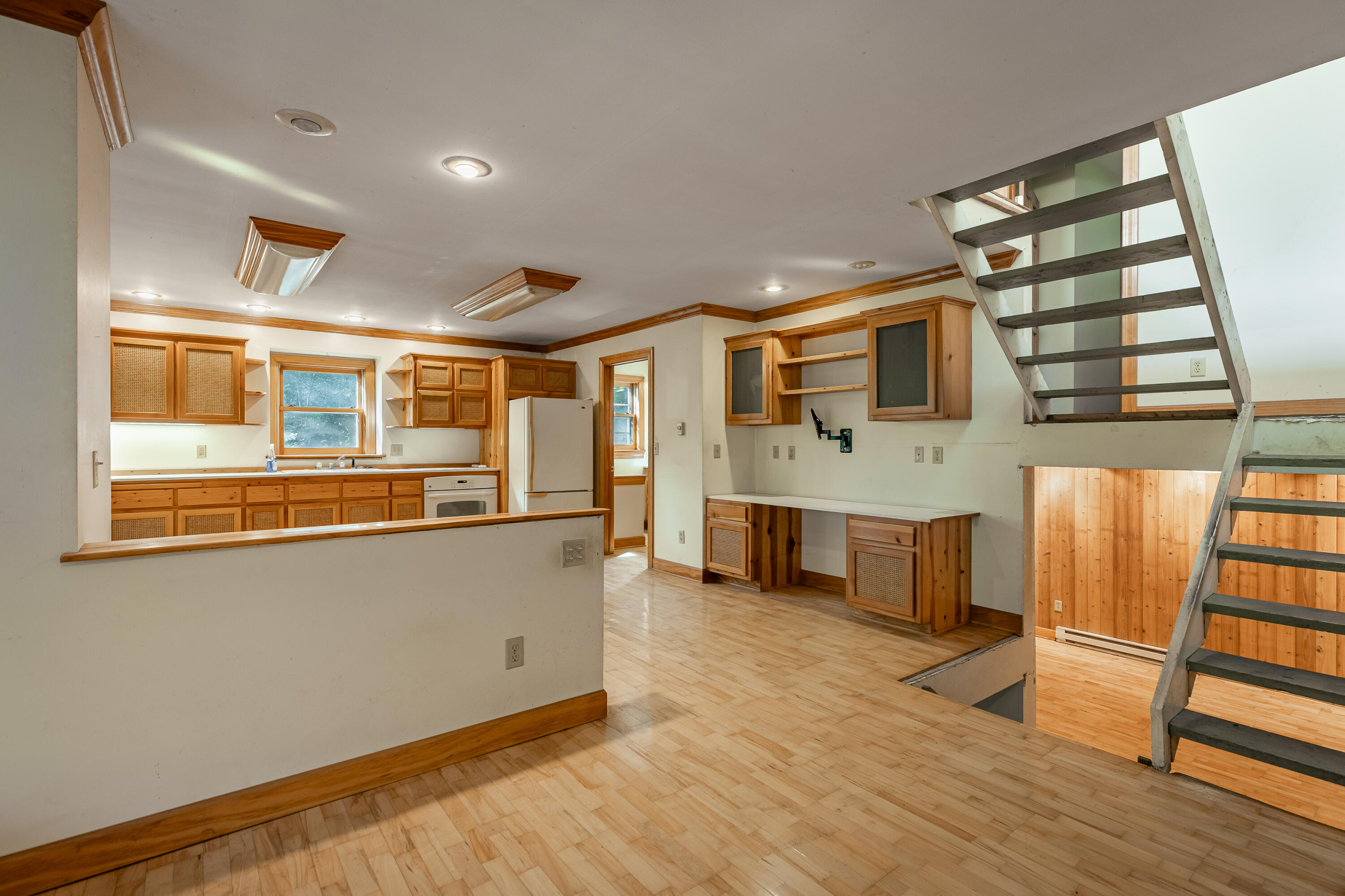 Kitchen with wood cabinetry and flooring, a long peninsula, and an open staircase to the lower level.