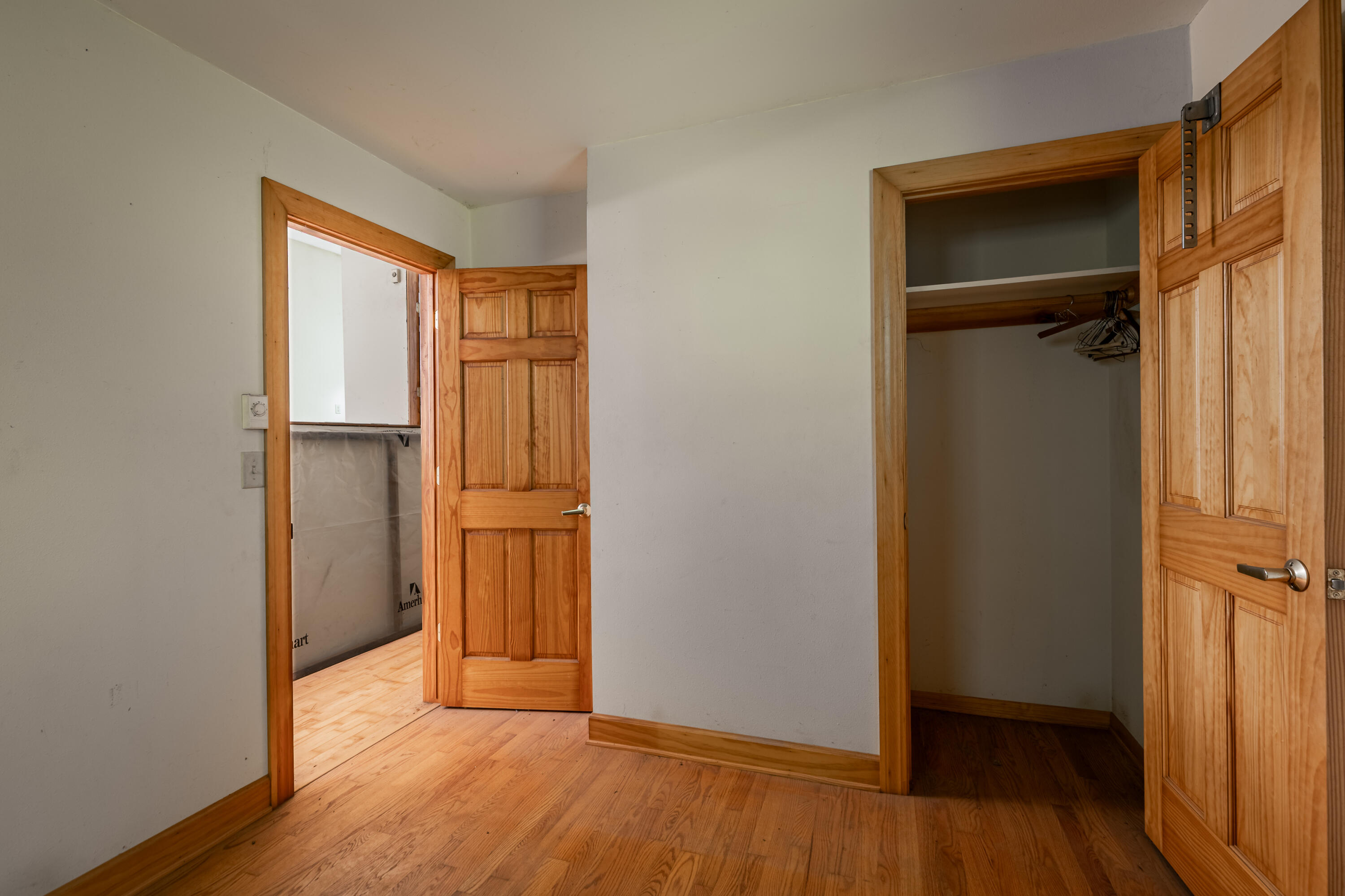 Empty room with hardwood floors and an open closet beside a doorway to a bright adjoining room.