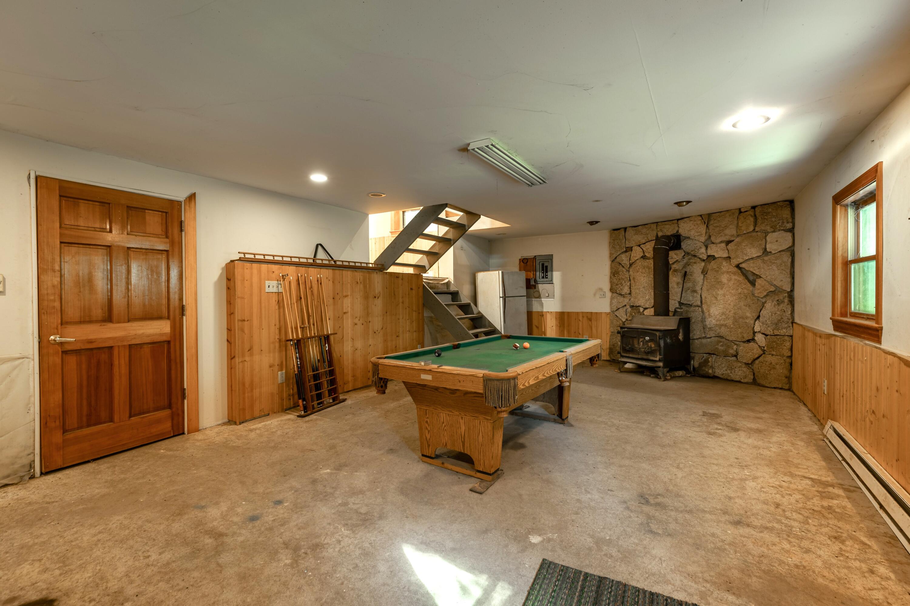 Basement recreation room with a pool table and wood-burning stove against a stone wall.