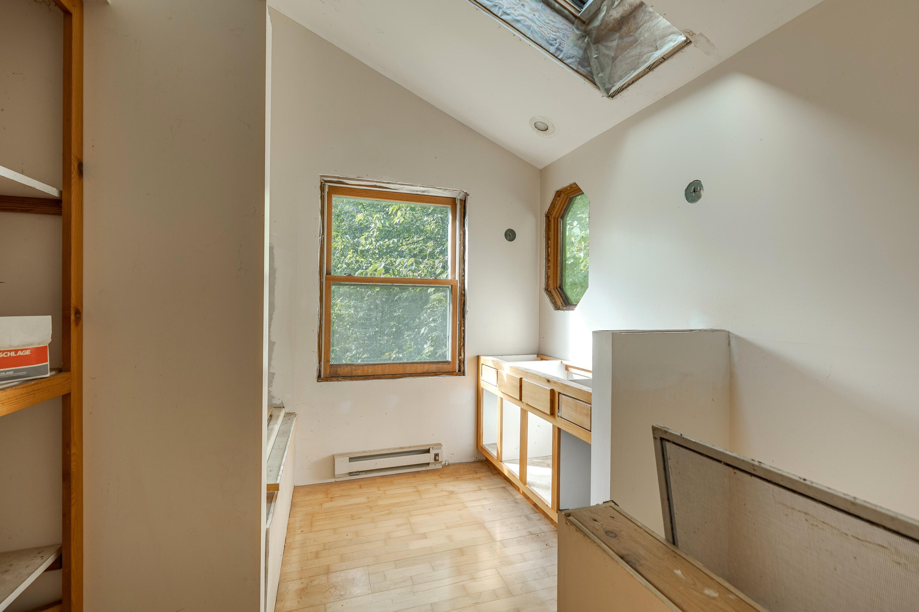Unfinished bathroom with skylight, wood-trimmed windows, and exposed vanity framing.
