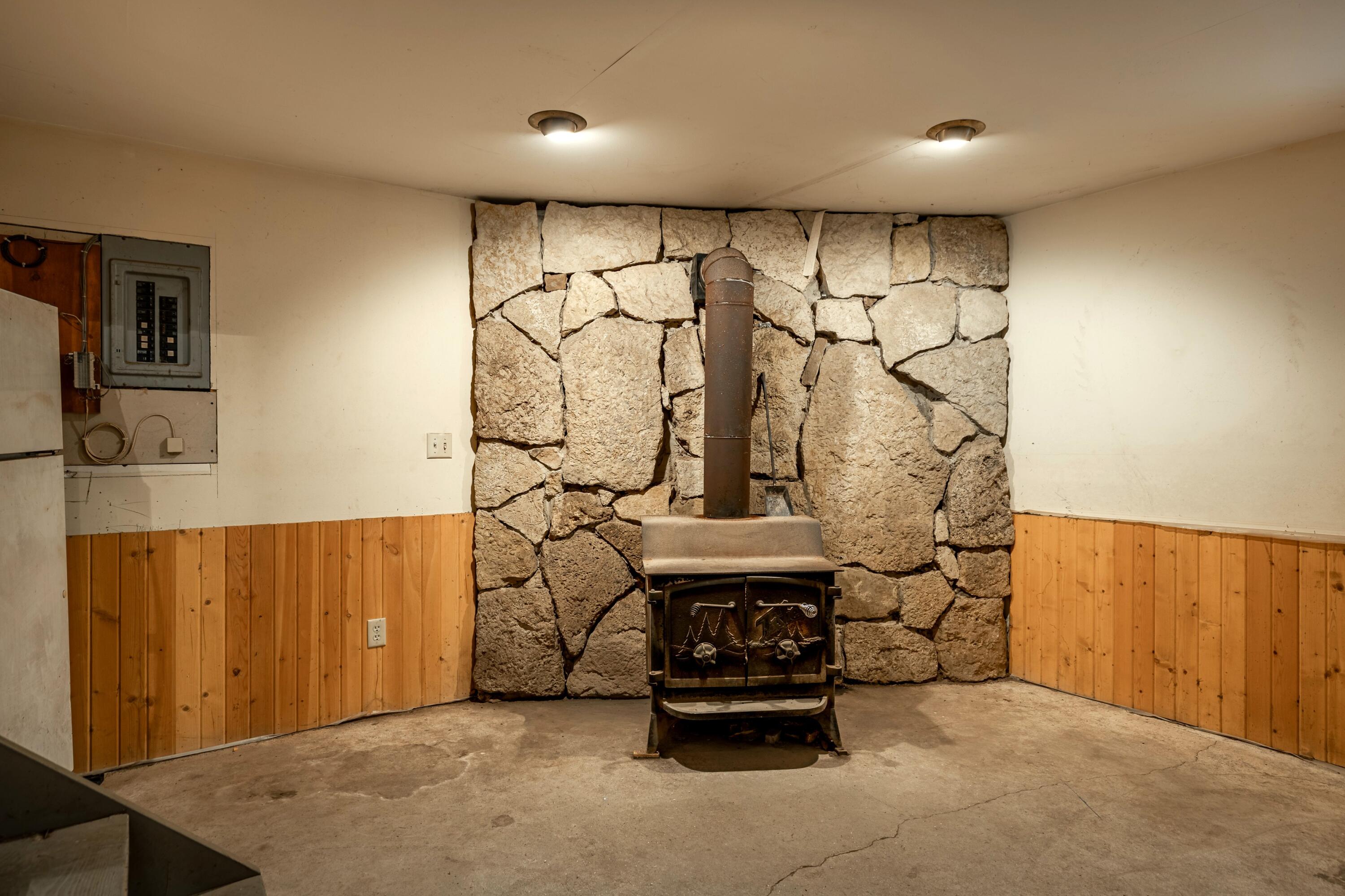 Basement wood stove in front of a rough stone wall, with wood paneling and concrete floor.