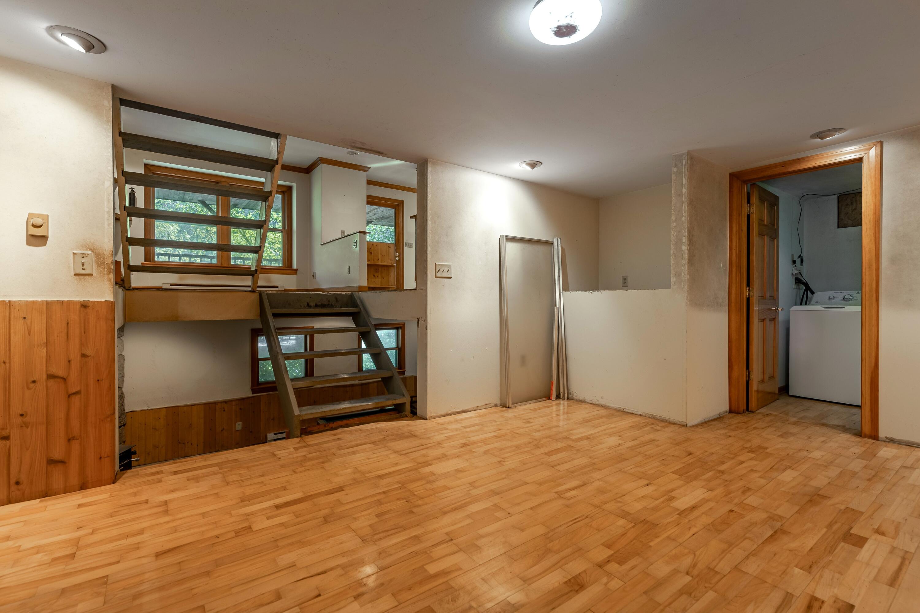 Empty room with wood flooring, an open staircase to a raised level, and a laundry room doorway.