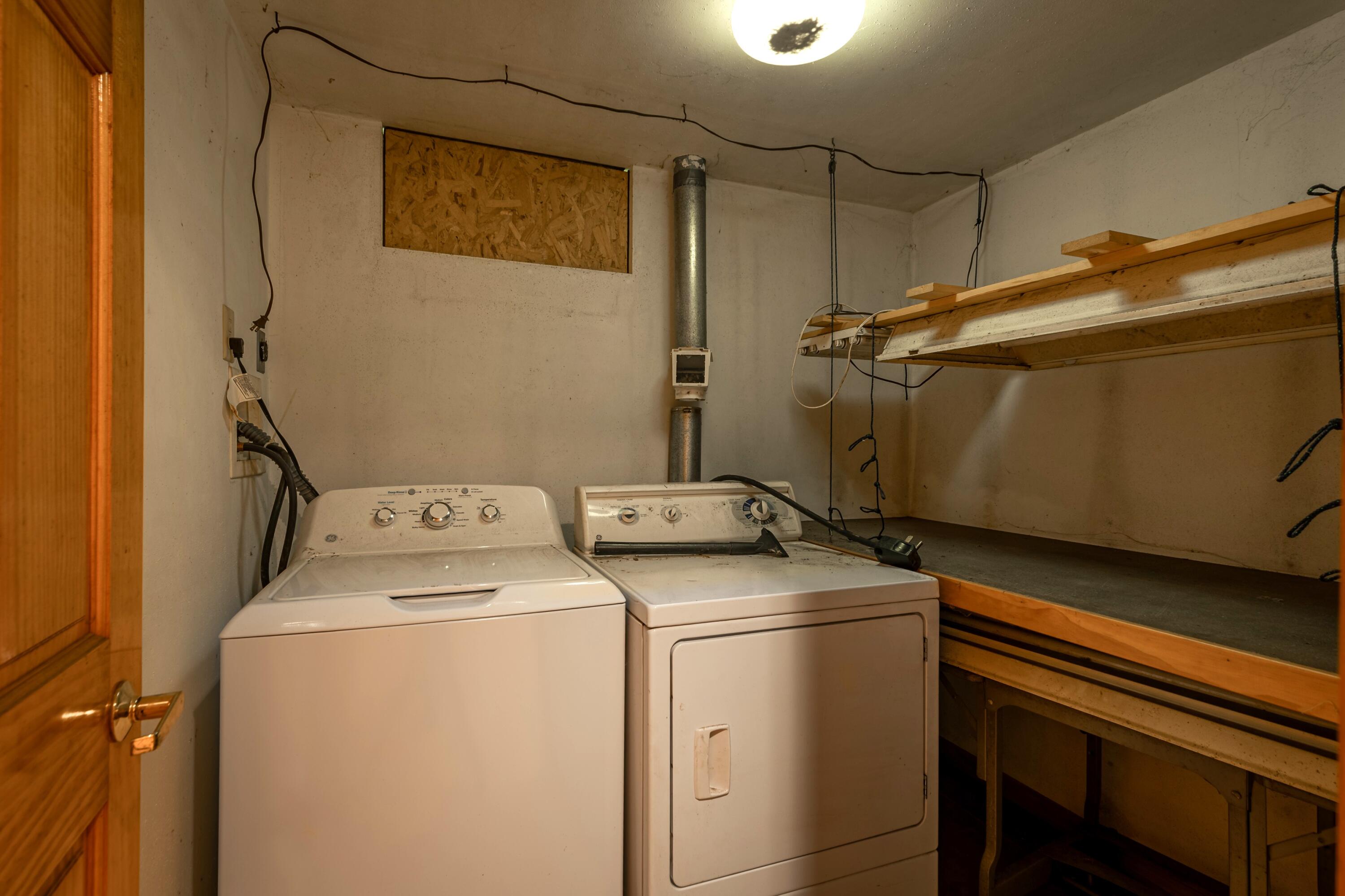 Laundry room with washer and dryer beside a long built-in workbench and overhead shelves.