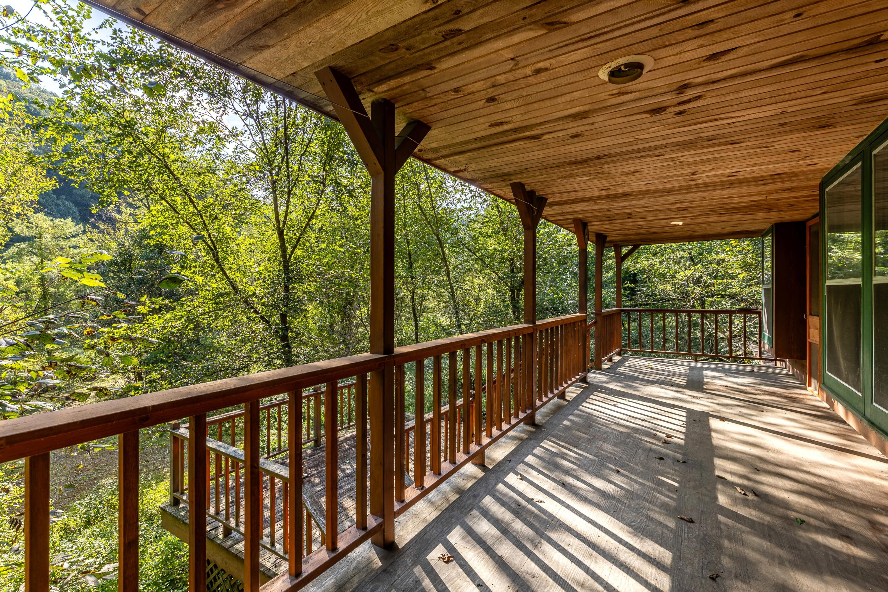 Covered wooden deck beside the home, overlooking dense green woods.