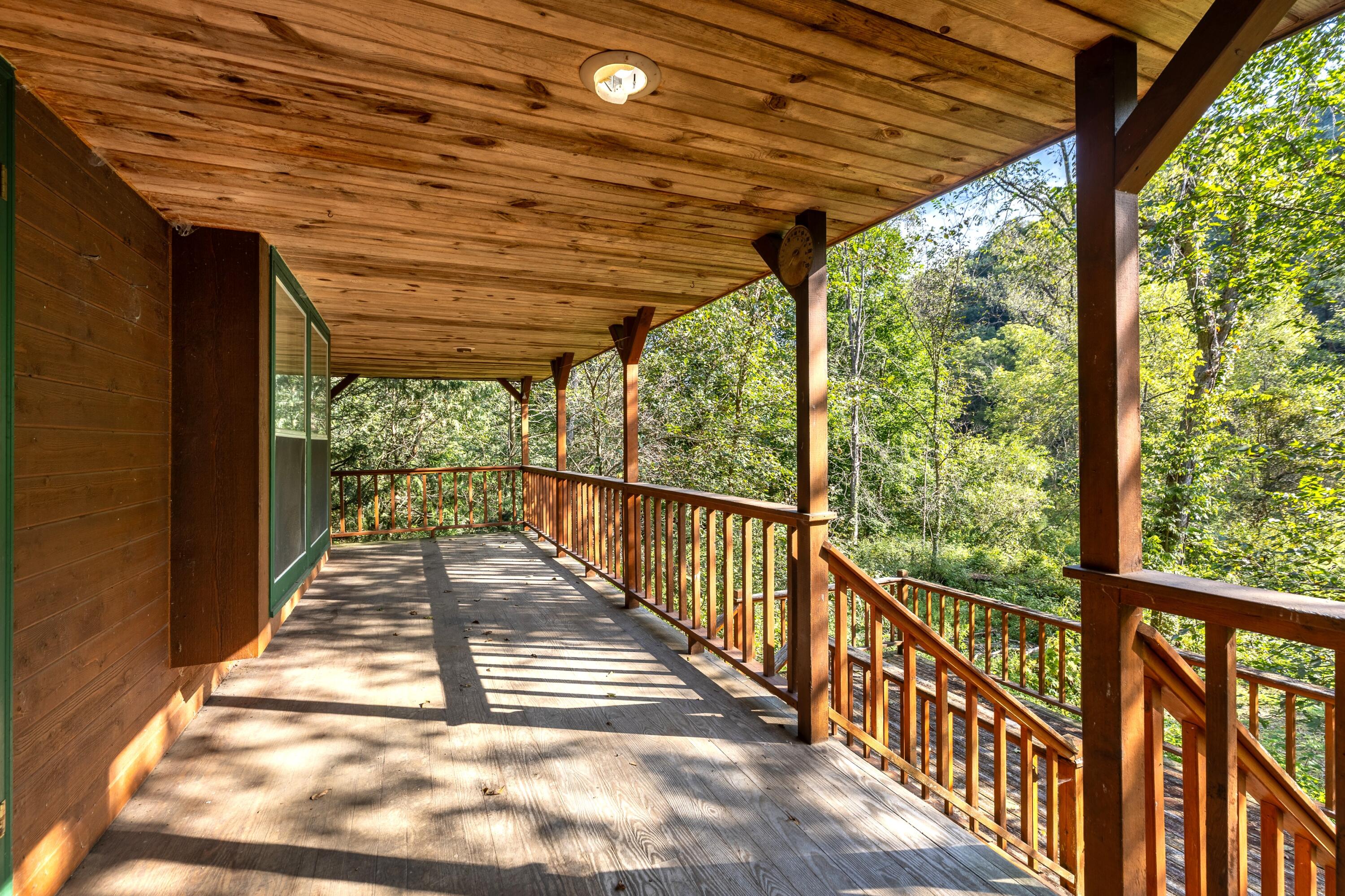 Covered wooden porch overlooking trees, with timber posts, railings, and stairs.