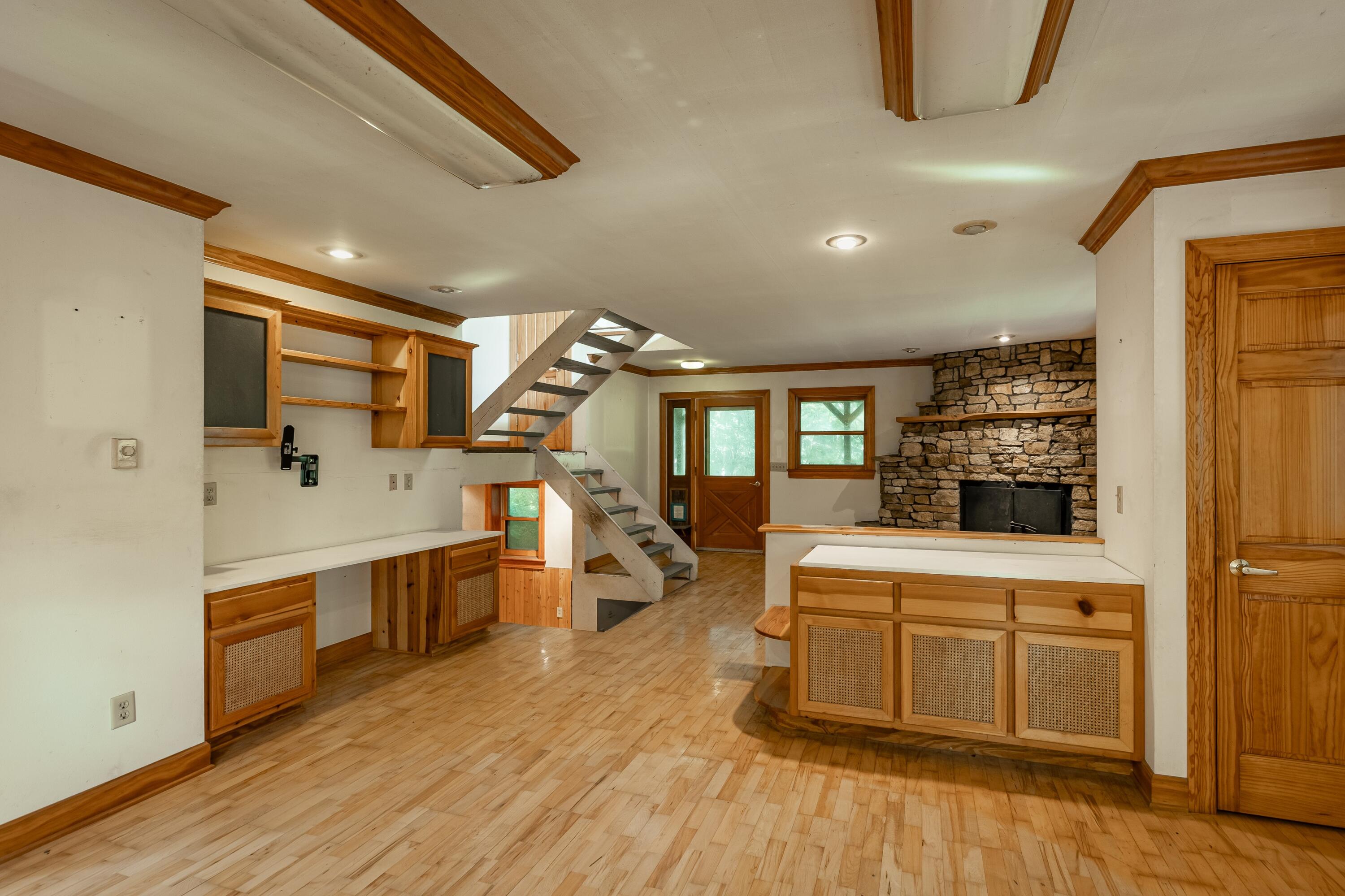 Open living area with wood cabinetry, an exposed staircase, and a large stone fireplace.