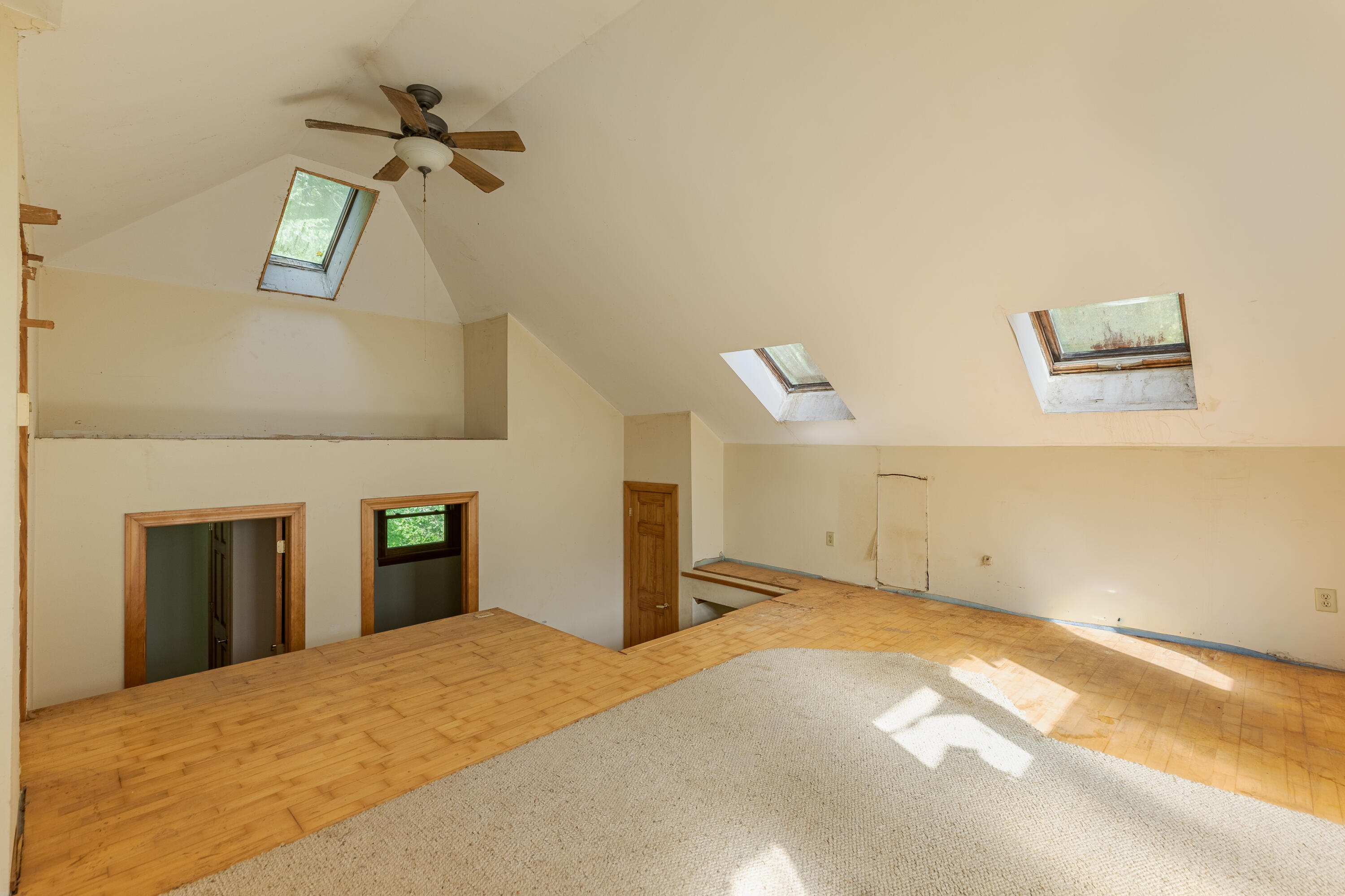 Vacant loft with multiple skylights, hardwood floors, and a carpeted area beneath a sloped ceiling.