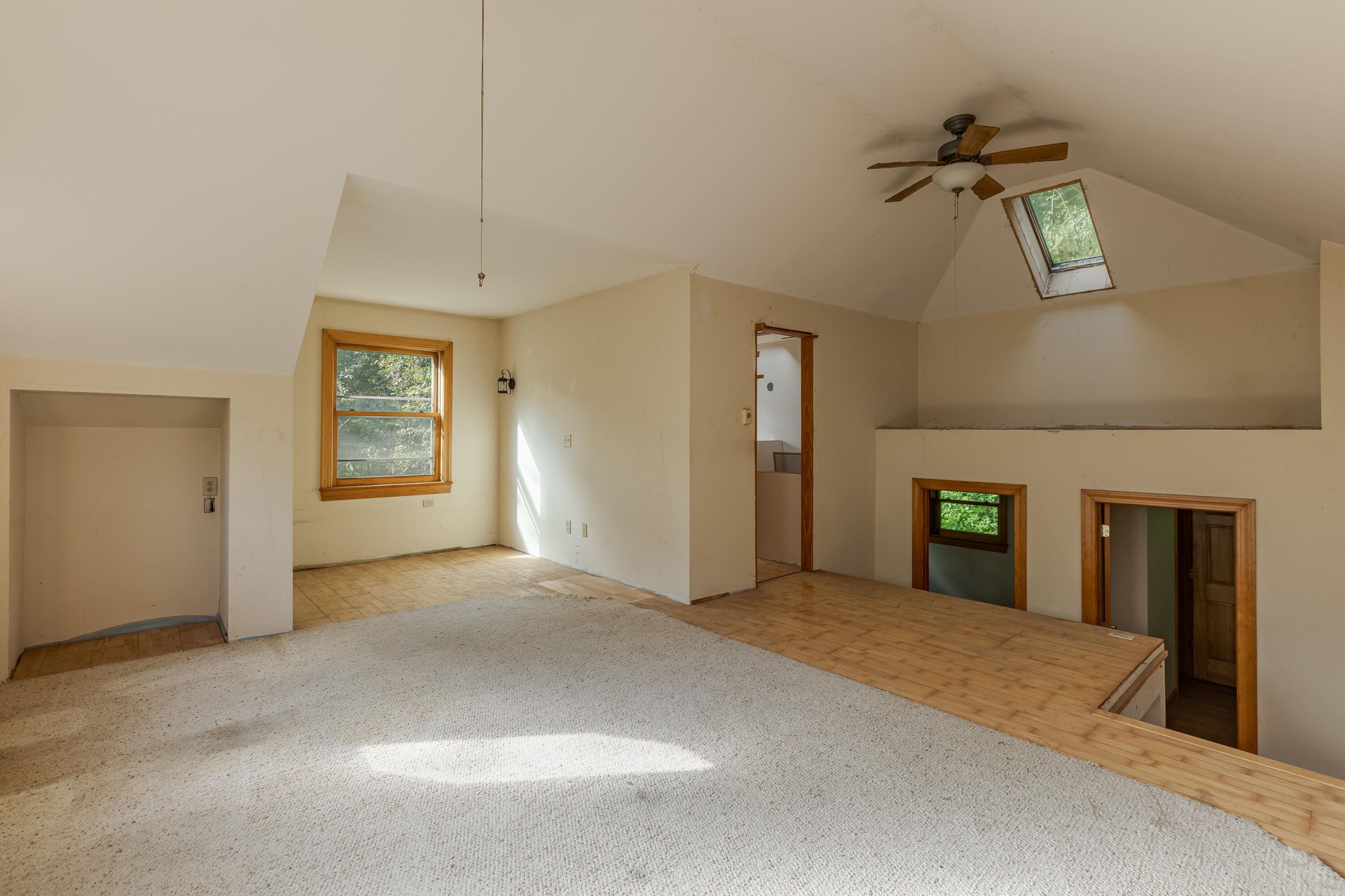 Empty upper-level room with sloped ceilings, a skylight, ceiling fan, and raised wood-floored area.