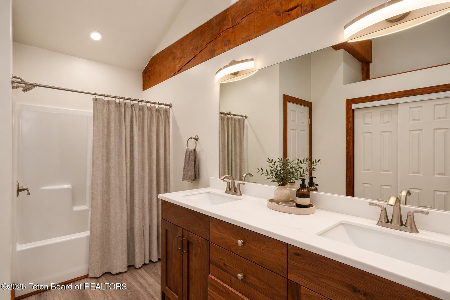 Bathroom with a double-sink wood vanity, large mirror, and curtained tub-shower.