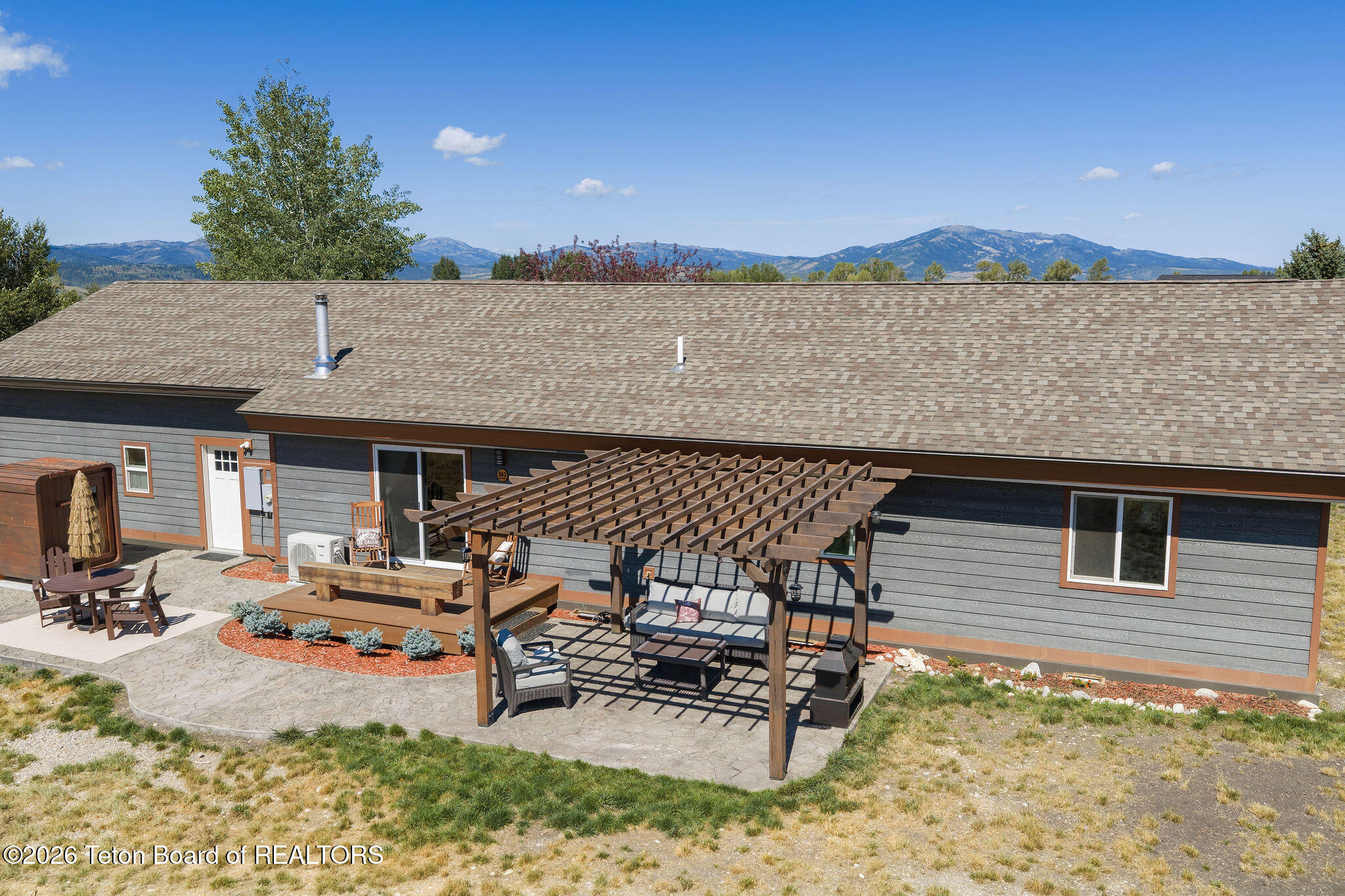 Gray home with a pergola-covered patio, outdoor seating, and mountains in the background.