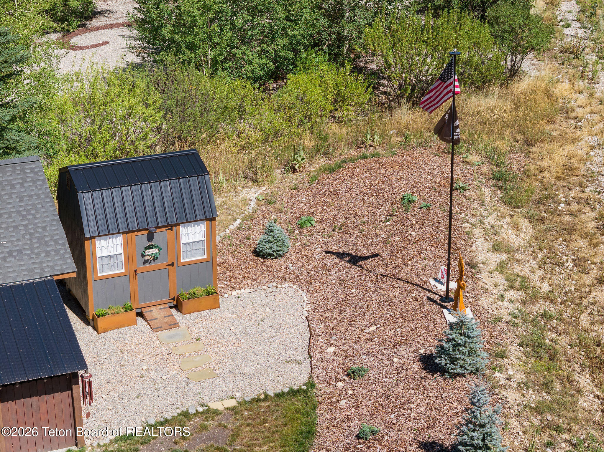 Small gray-and-orange shed beside gravel paths and a flagpole flying an American flag.