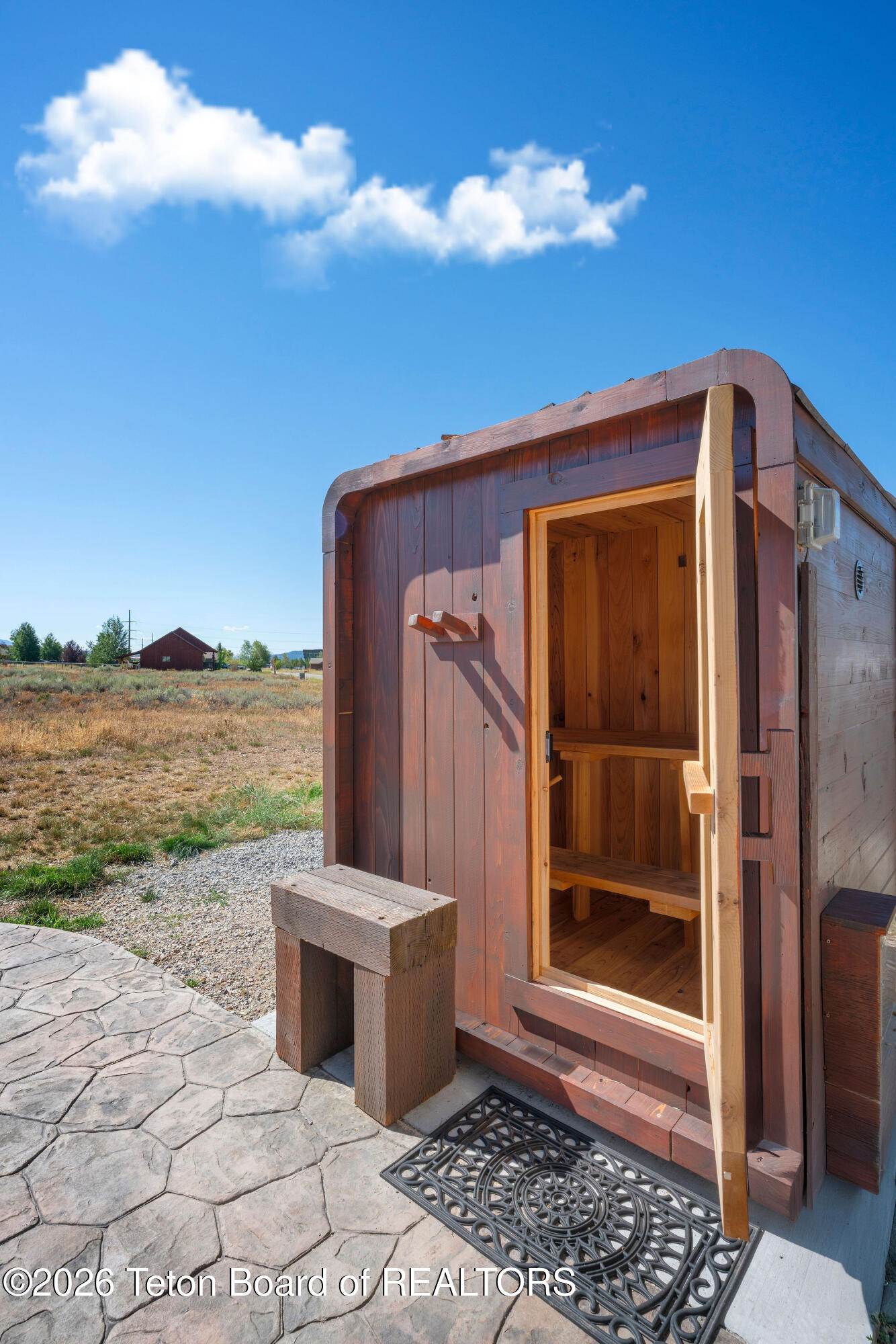 Wooden outbuilding with an open doorway revealing built-in benches beside a stamped-stone patio.