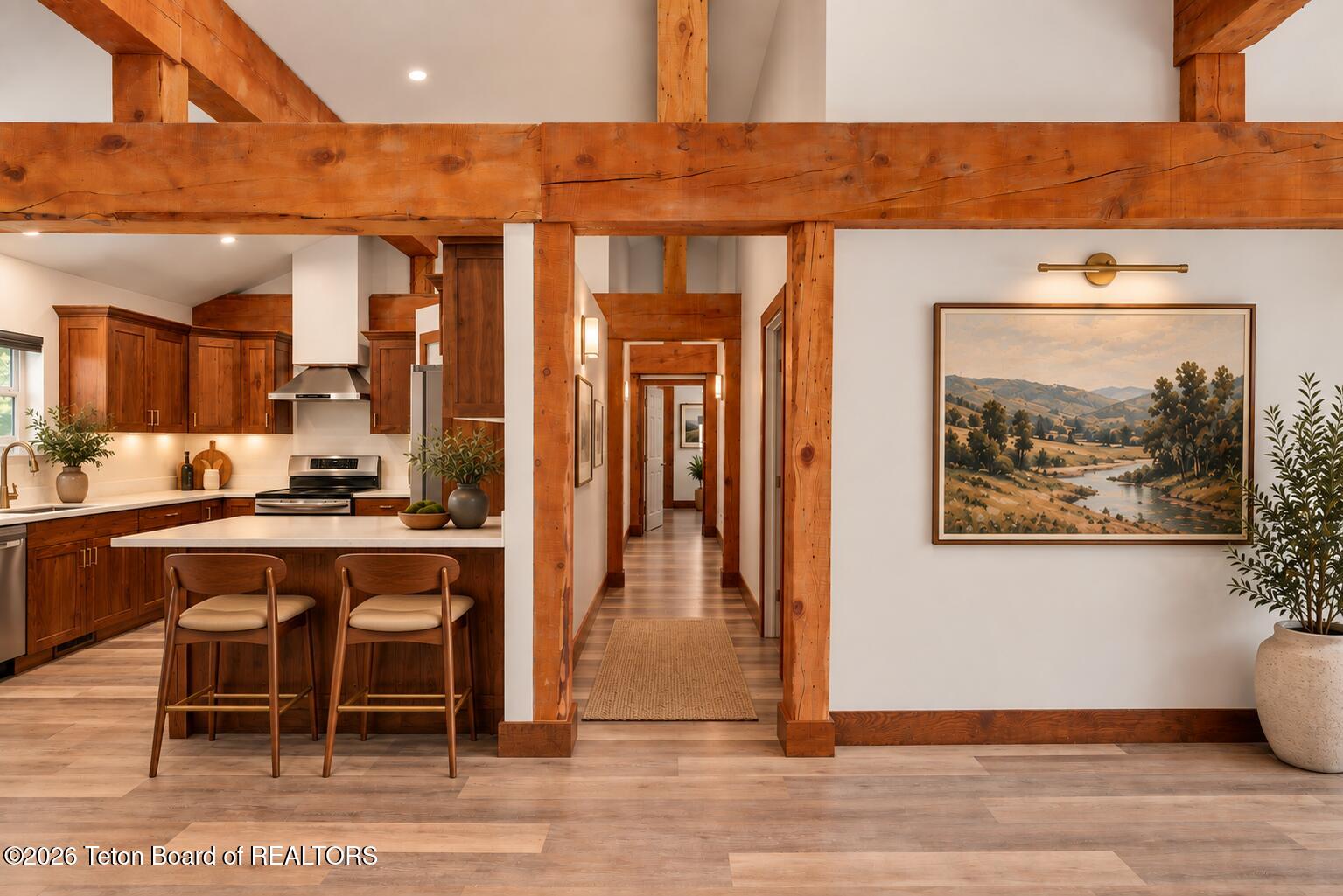 Warm wood kitchen with island seating, exposed timber beams, and a hallway beyond.